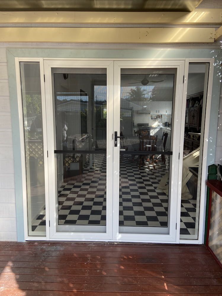 A White Door With A Checkered Floor Is Sitting On A Wooden Deck — Browny's Glass & Aluminium in Wingham, NSW