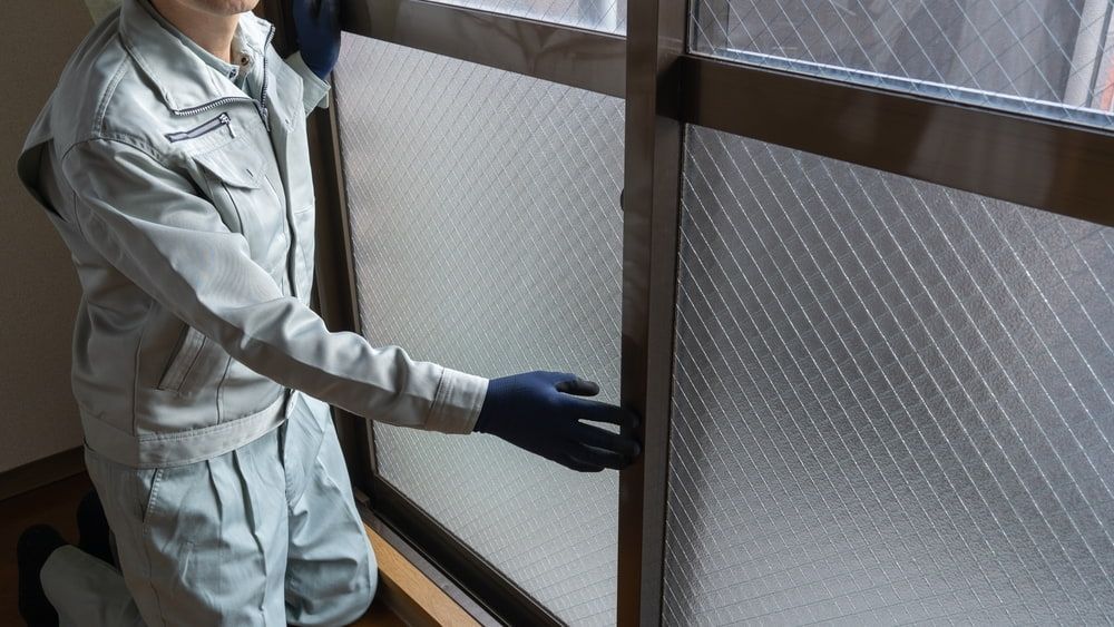 A Man Is Cleaning A Window With A Cloth And Gloves — Browny's Glass & Aluminium in Taree, NSW