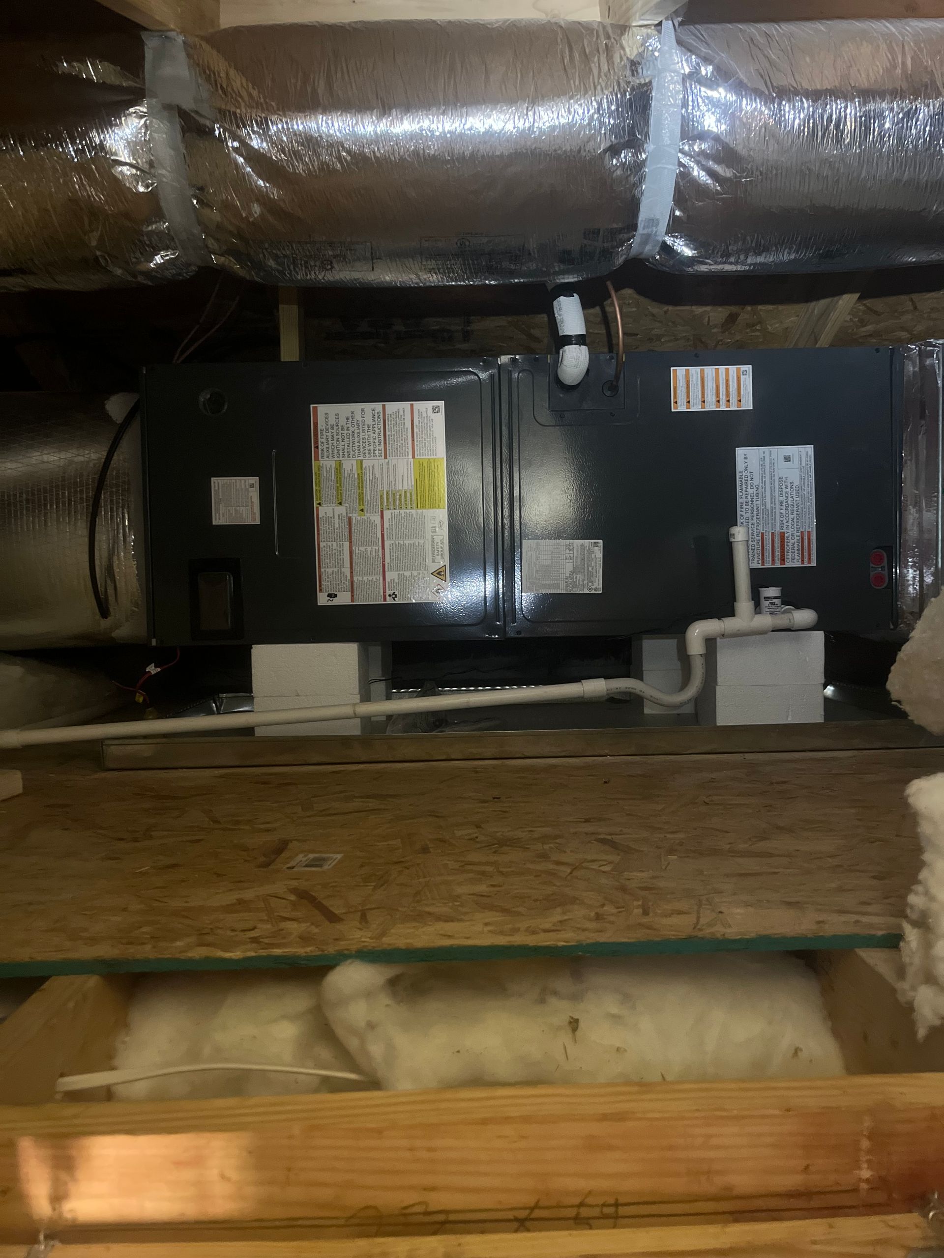 HVAC unit in a crawl space, black box with ductwork and insulation, mounted on wooden supports.