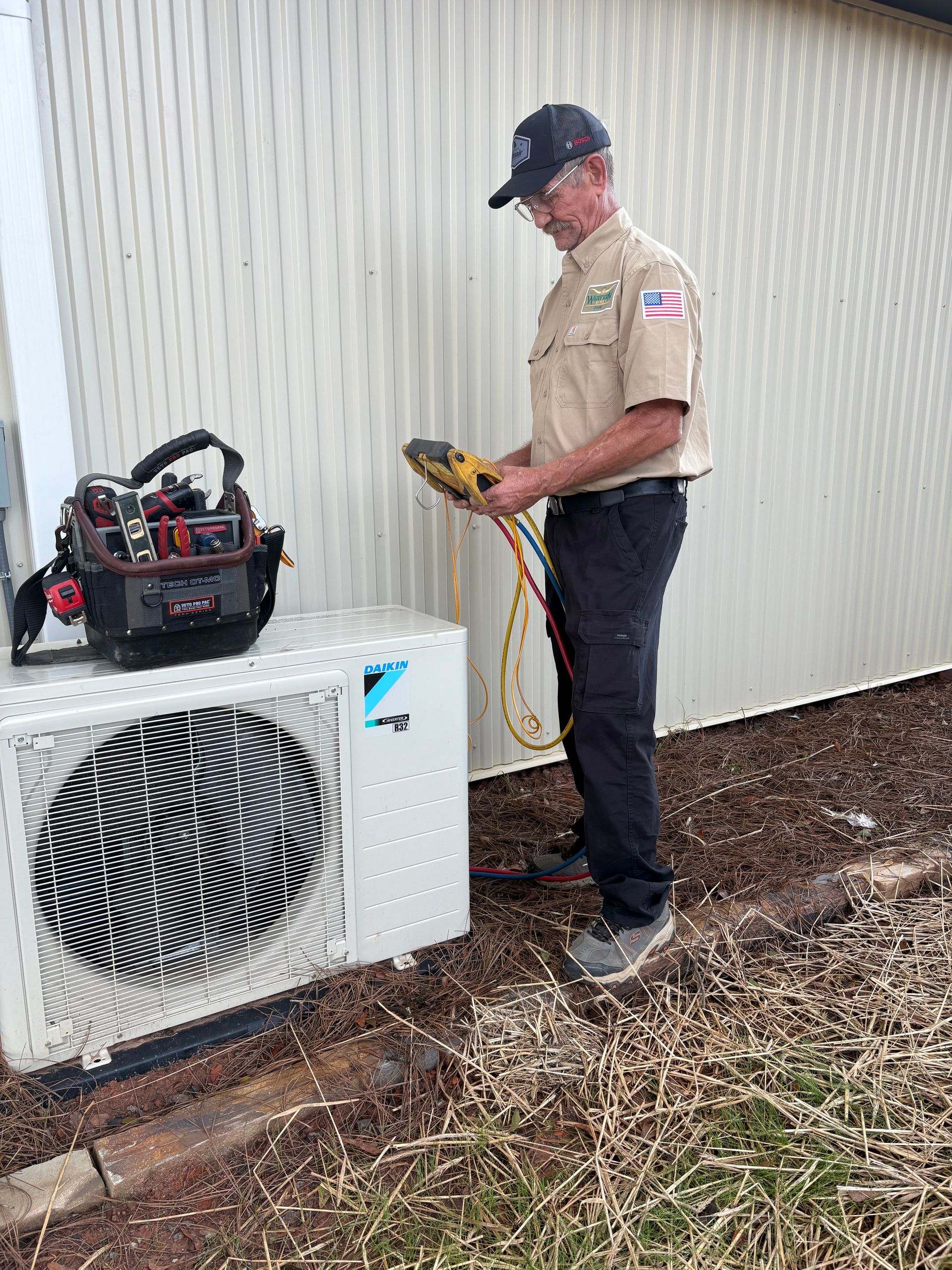 HVAC technician in uniform using a gauge on an outdoor AC unit; tools nearby.