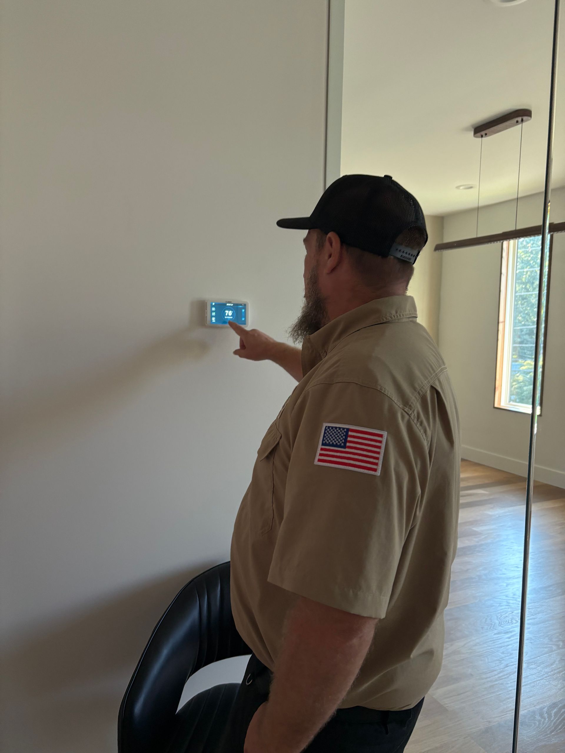 Man pointing at a blue thermostat on a beige wall indoors.