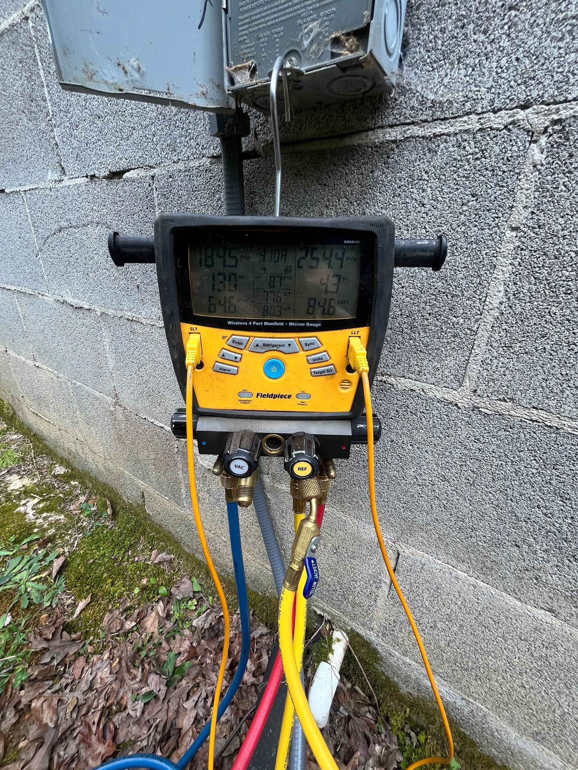 Yellow refrigerant gauges attached to an AC unit, displaying readings.