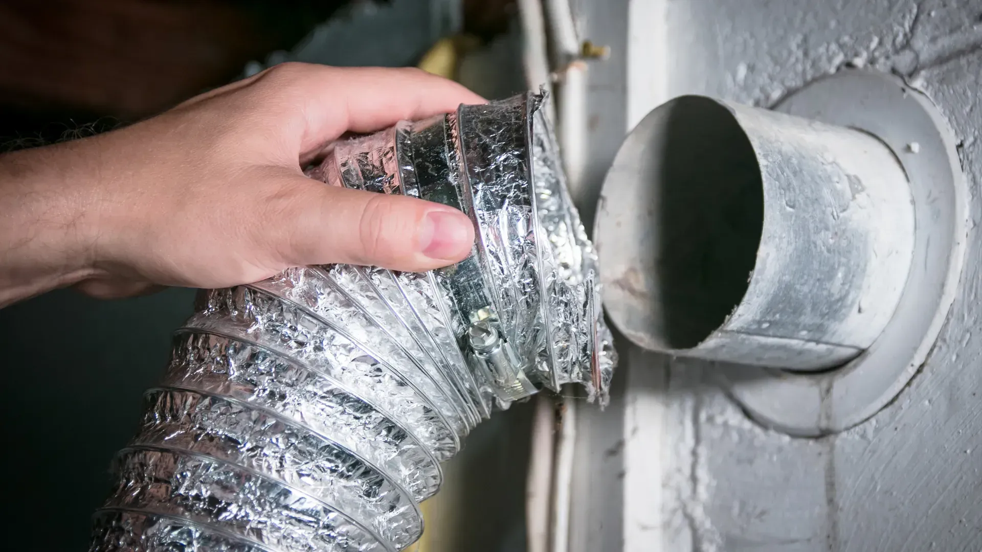 A person is holding a hose that is coming out of a hole in a wall.