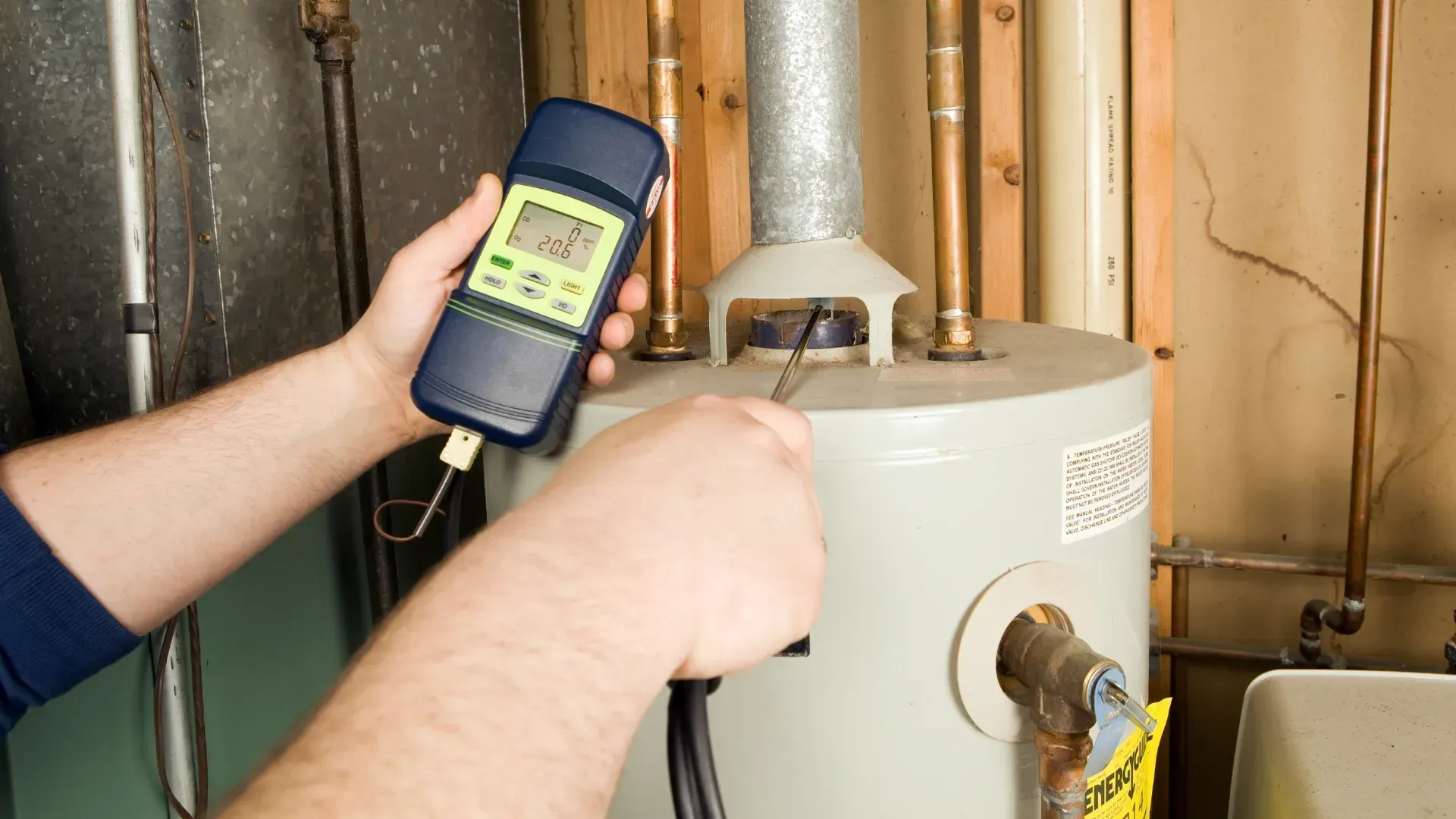 A person is holding a thermometer in front of a water heater.