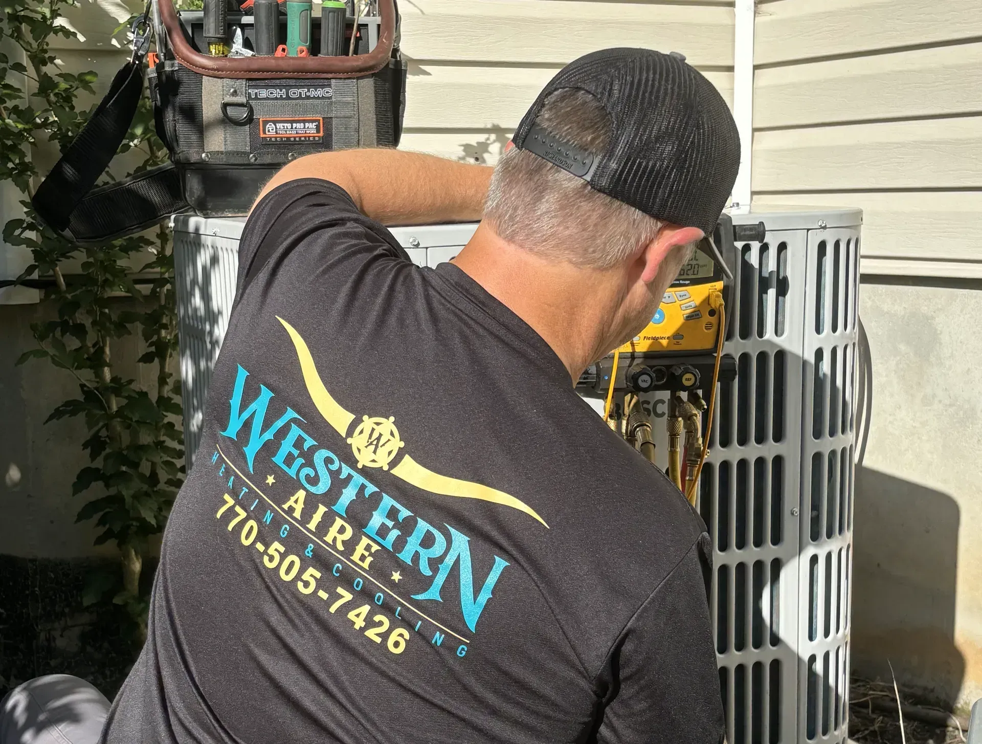 A man wearing a western aire shirt is working on an air conditioner.