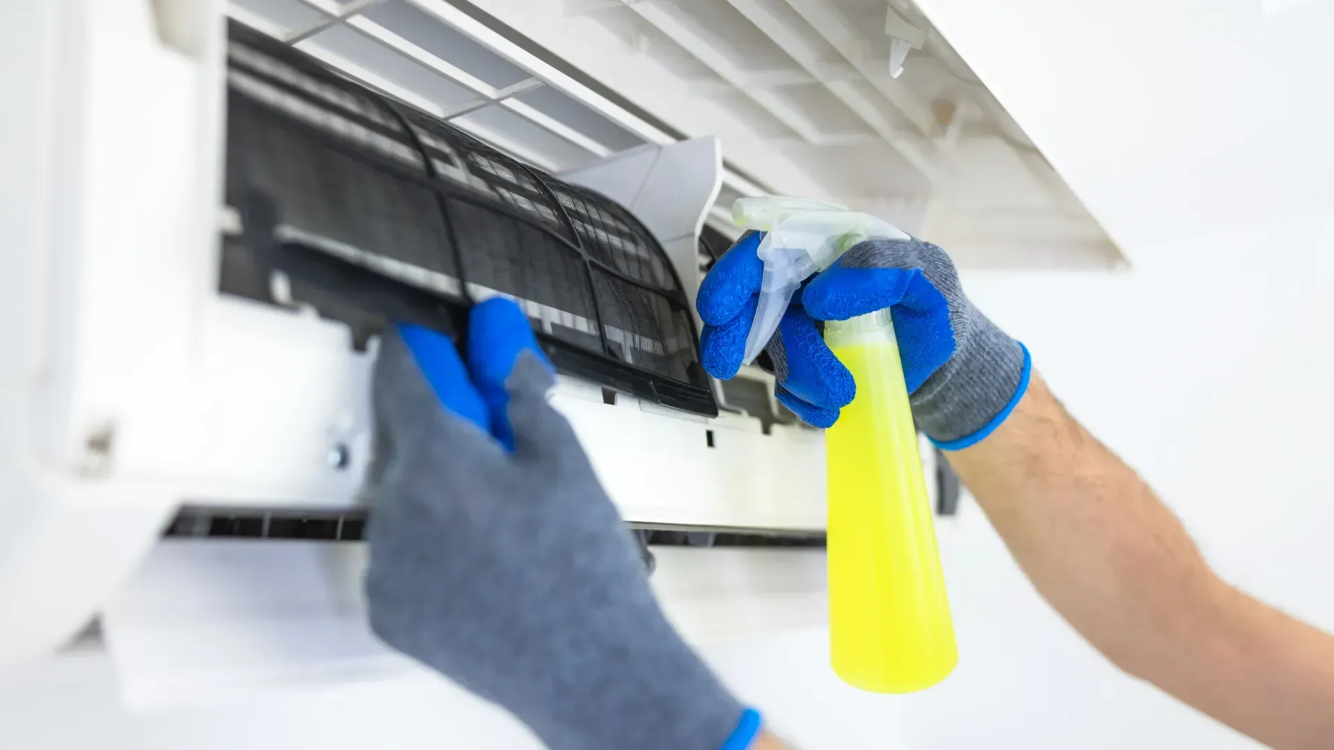 A person is cleaning an air conditioner with a spray bottle.