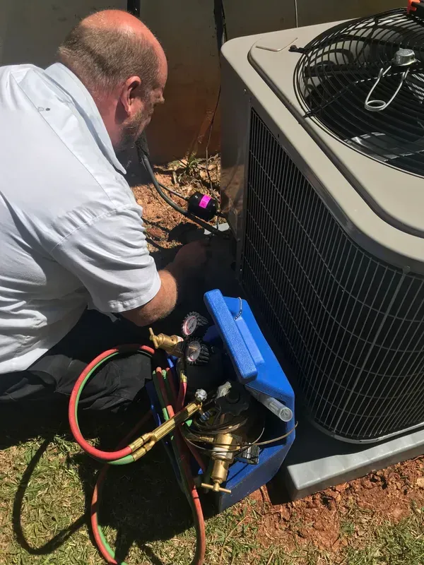A man is working on an air conditioner outside in the grass.