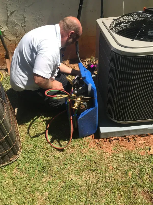 A man is kneeling down in front of an air conditioner.
