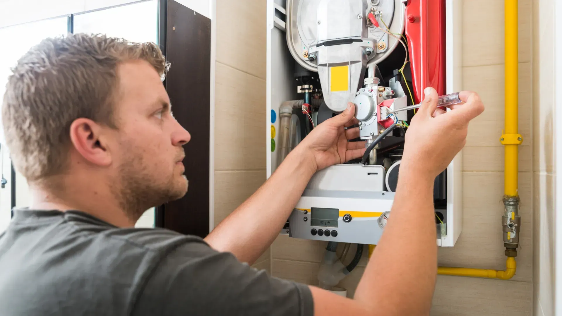 A man is fixing a boiler with a wrench.