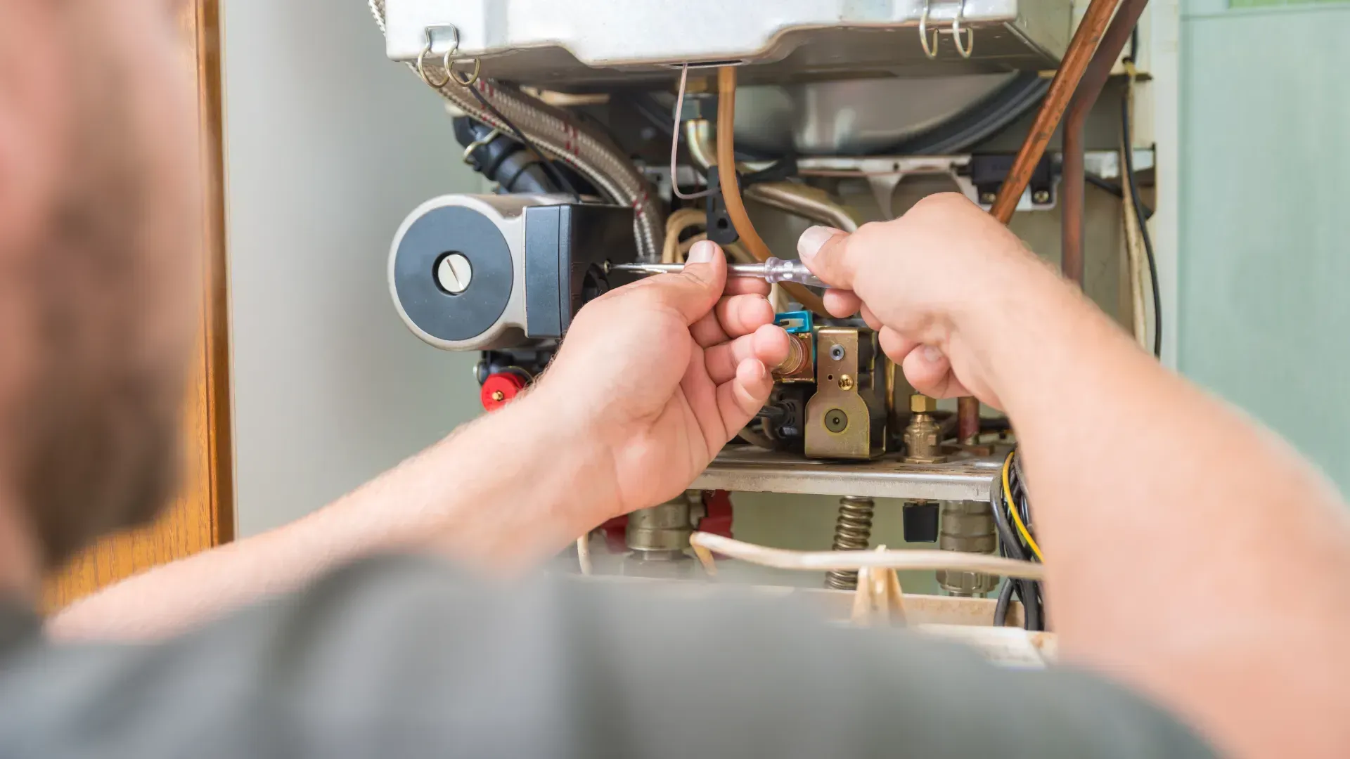 A man is fixing a boiler with a screwdriver.