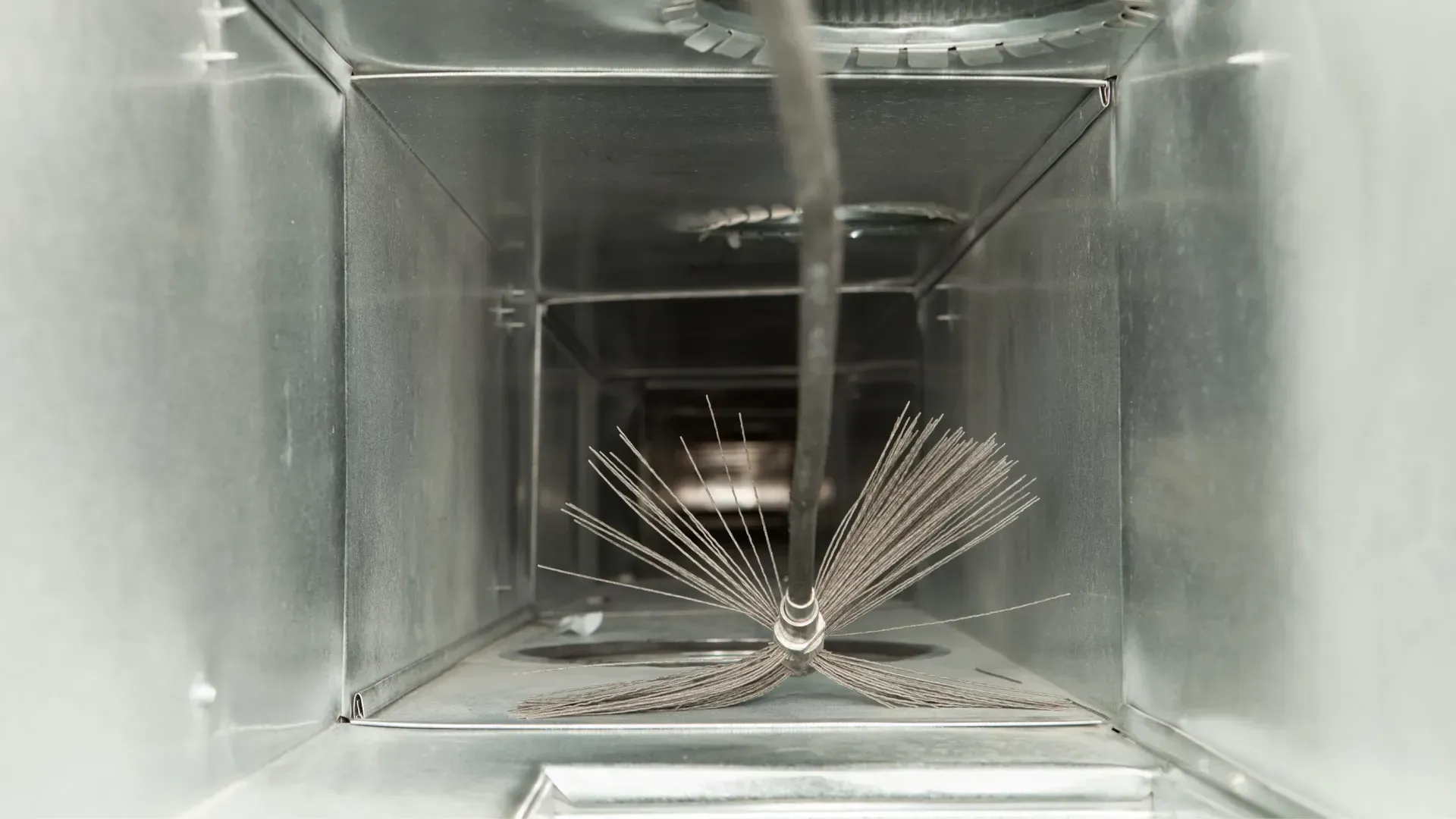 A brush is being used to clean an air duct.