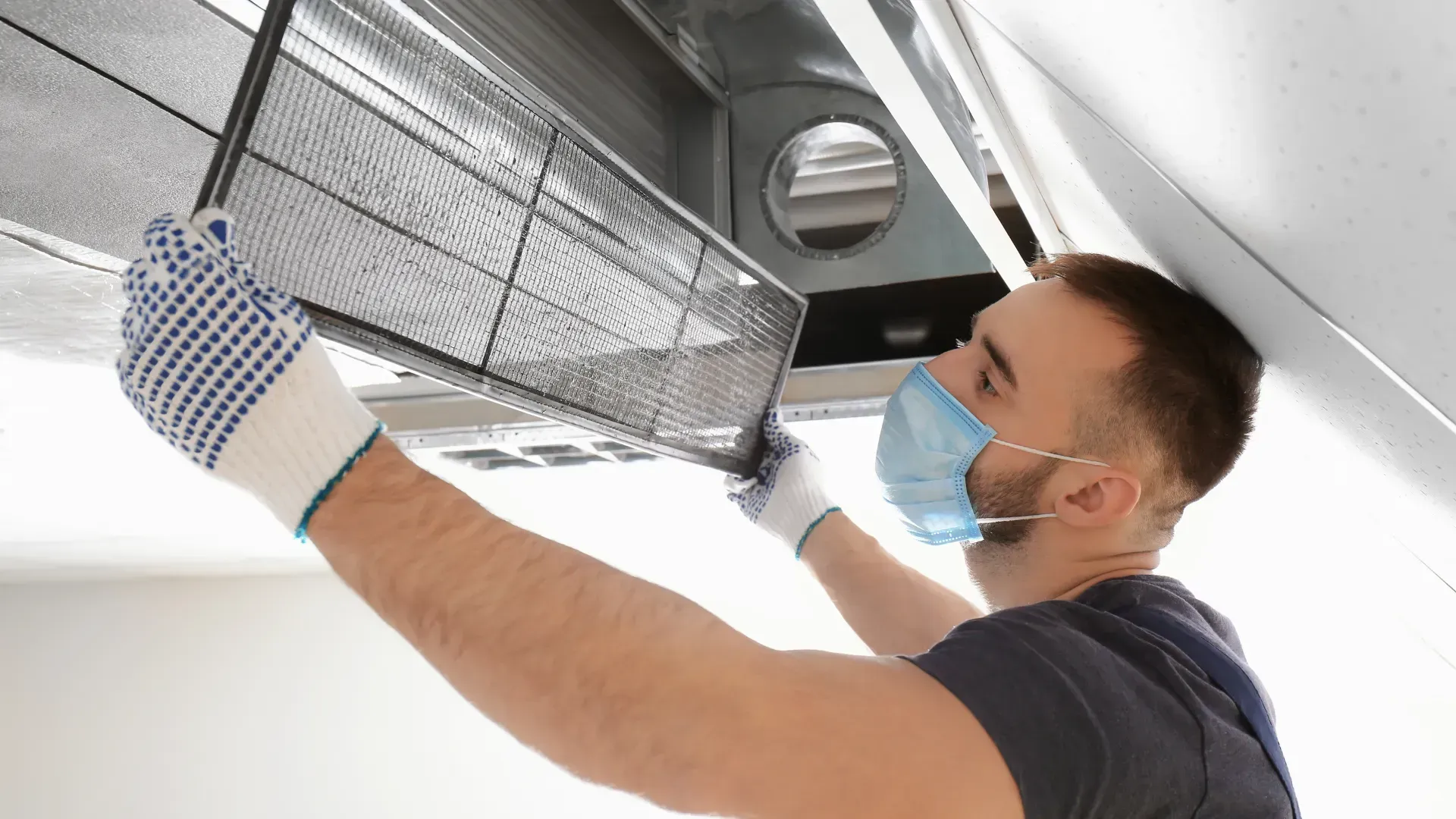 A man wearing a mask and gloves is cleaning an air conditioner.