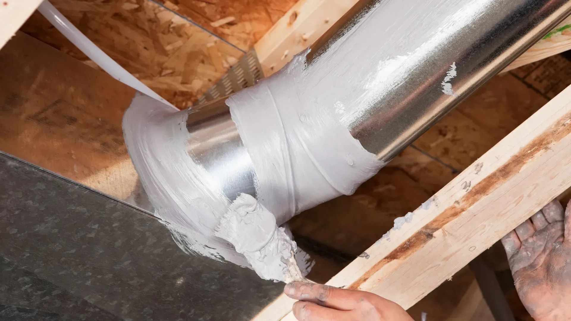 A person is painting a metal pipe with white paint.