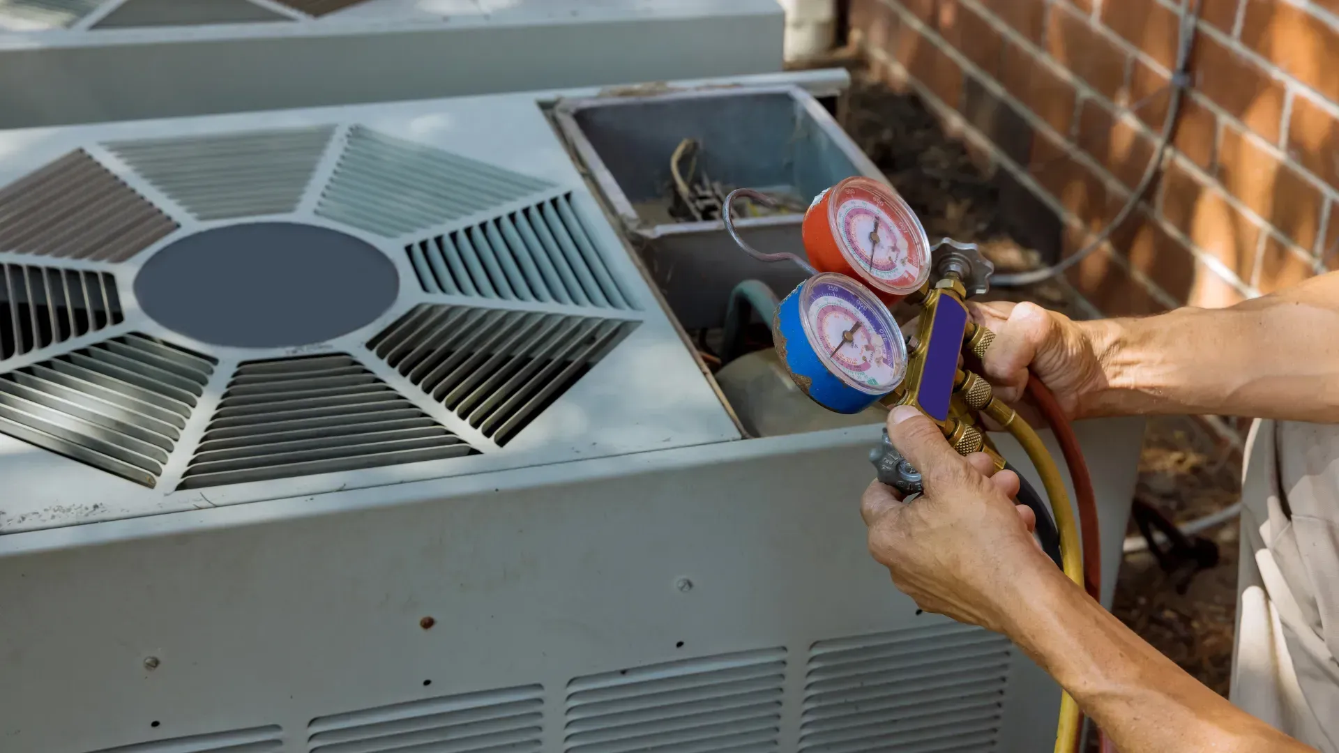 A man is working on an air conditioner outside of a brick building.