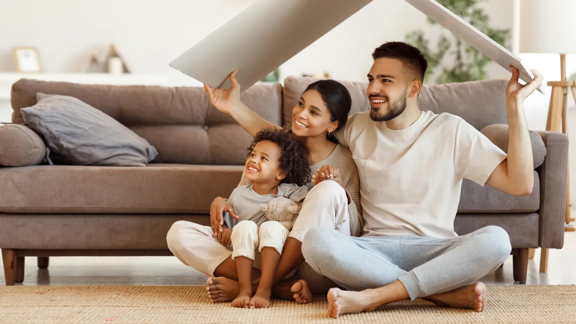 A family is sitting on the floor under a sheet of paper.
