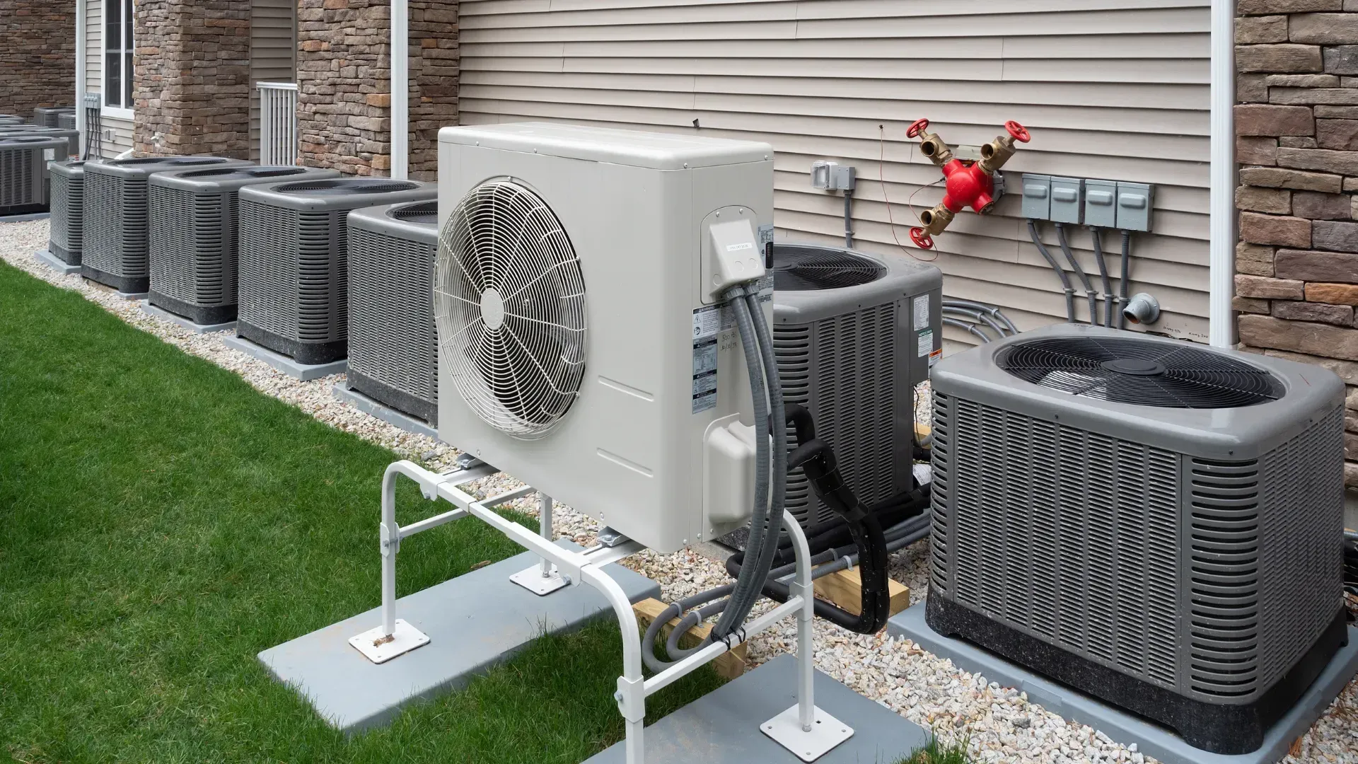 A row of air conditioners are sitting outside of a house.