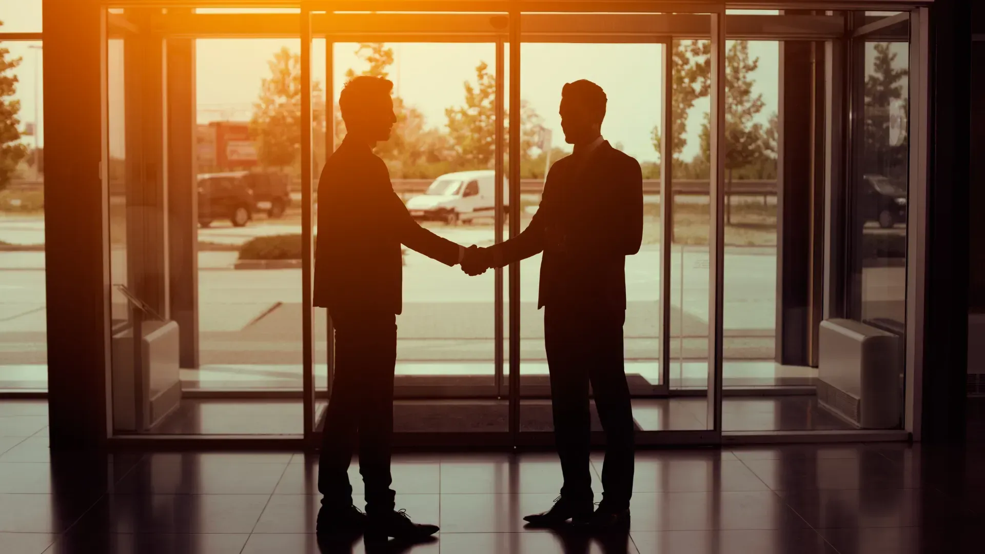 Two businessmen are shaking hands in front of a glass door.