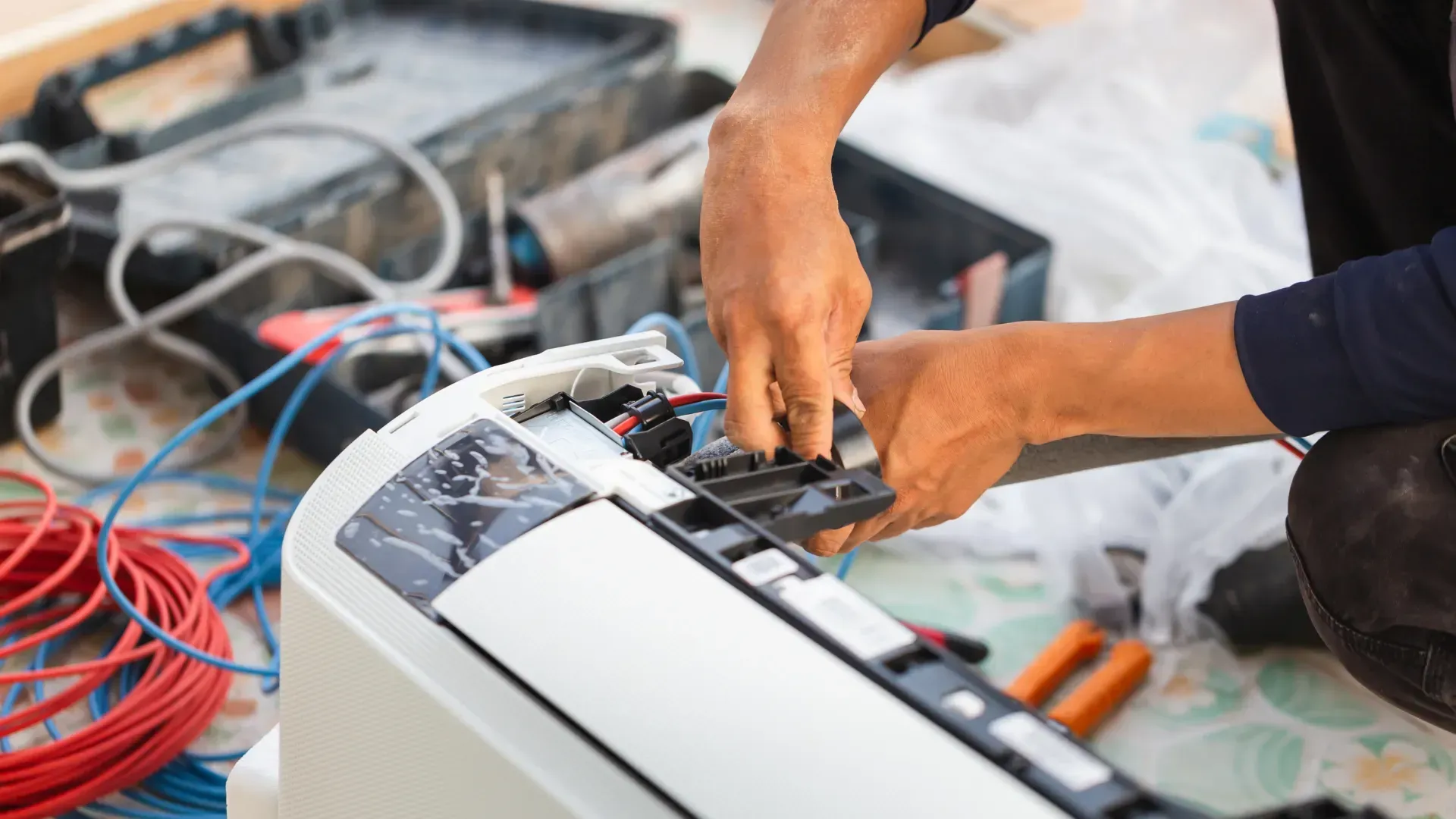 A man is fixing an air conditioner with a pair of pliers.