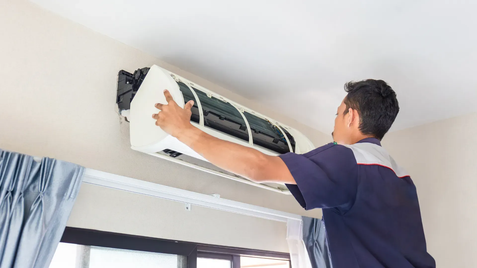 A man is cleaning an air conditioner in a living room.
