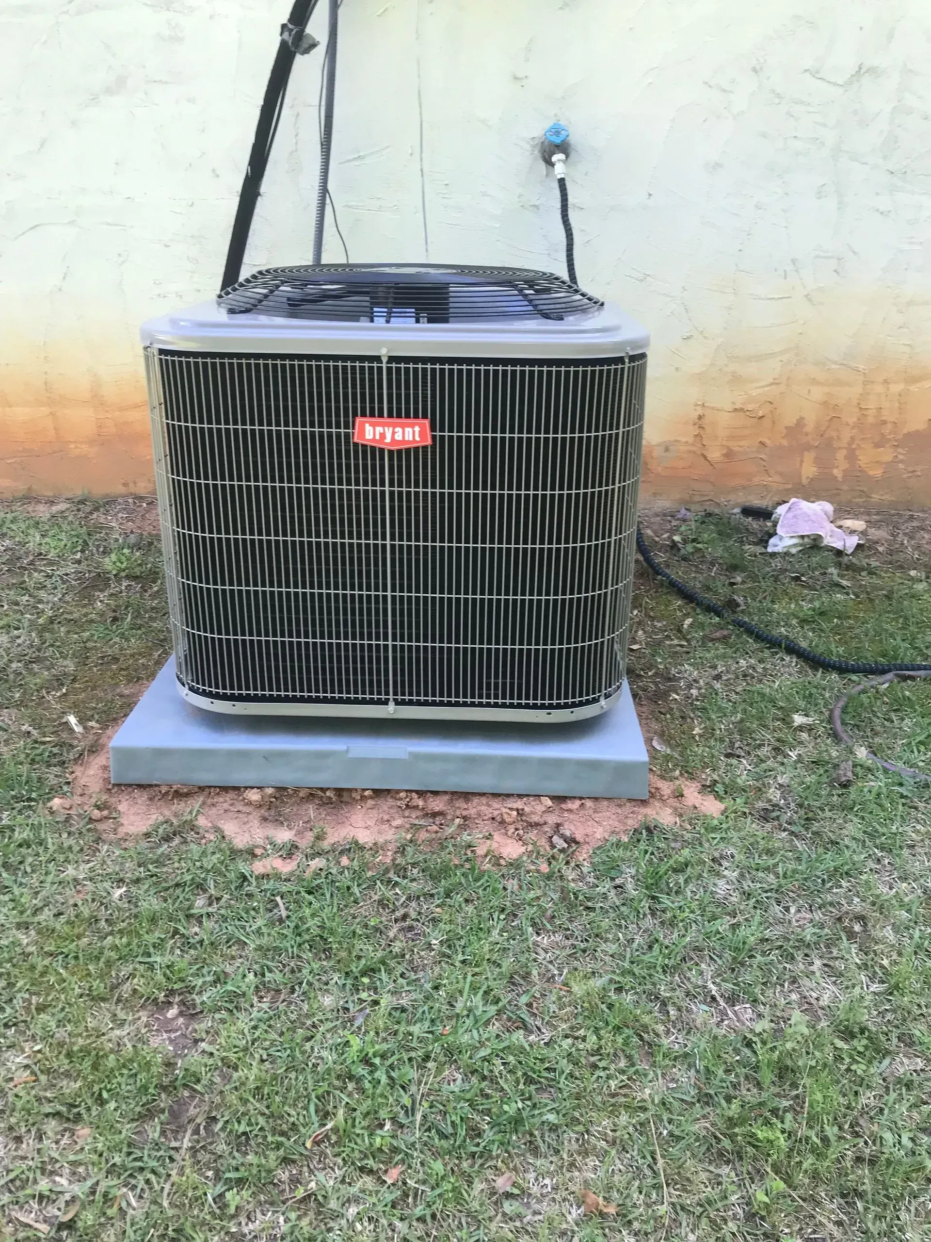 A large air conditioner is sitting in the grass next to a wall.