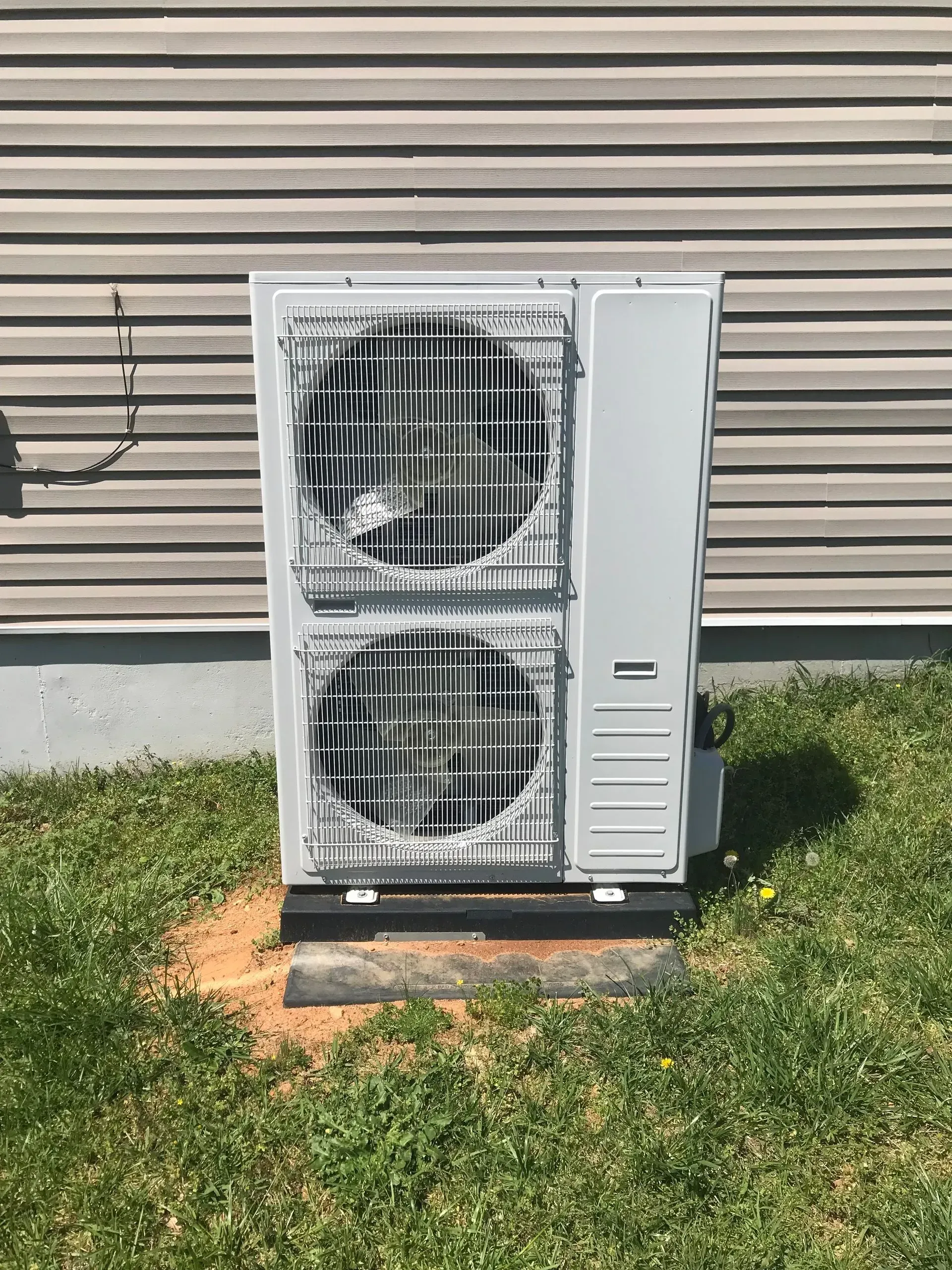 A white air conditioner is sitting in the grass in front of a house.