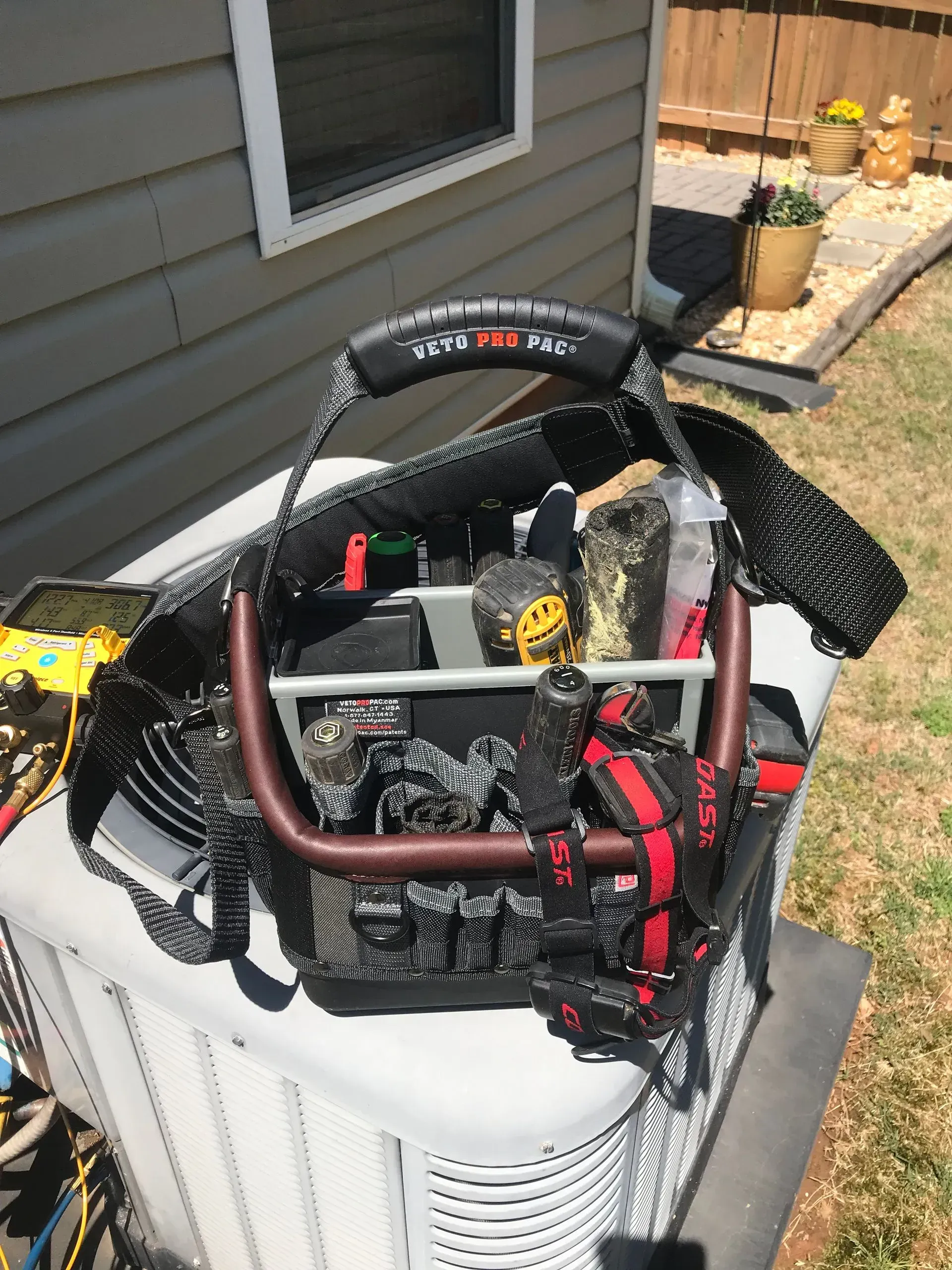 A tool bag is sitting on top of an air conditioner.