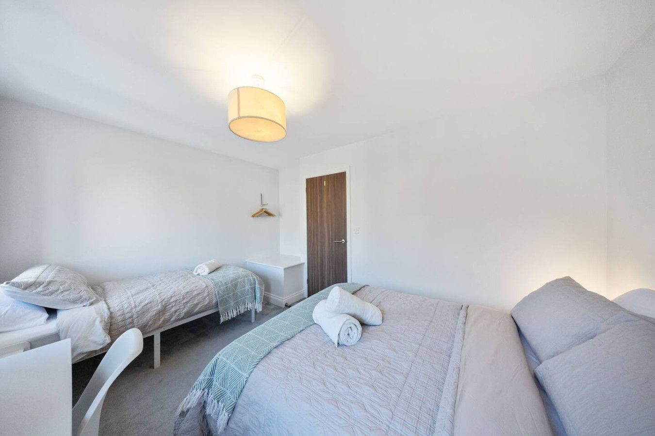 A hotel room with one queen bed, one twin bed, white walls, gray bedding, and a closed wooden door.