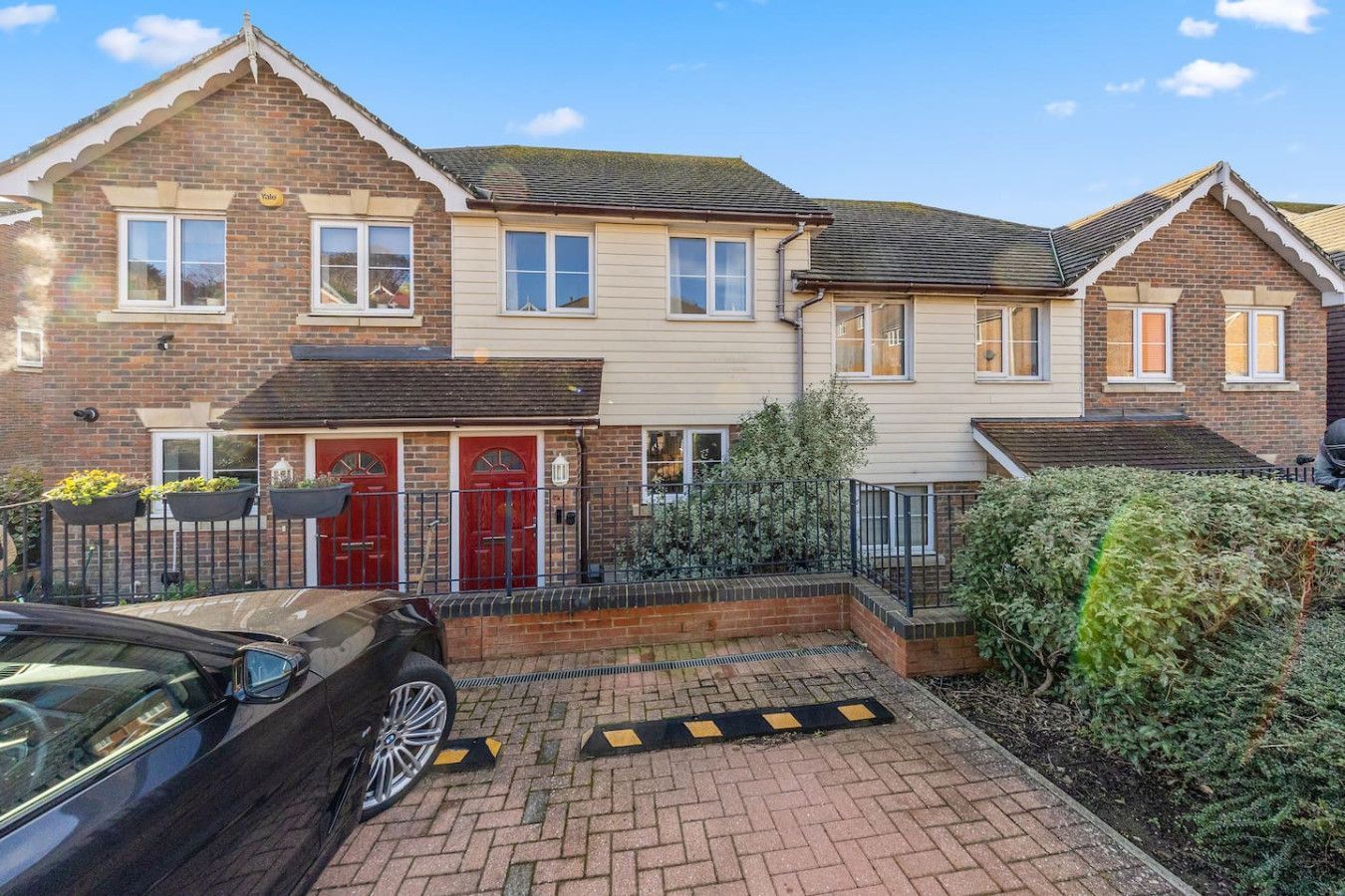 A row of brick and cream-colored townhouse-style homes with red doors and a paved driveway in front.