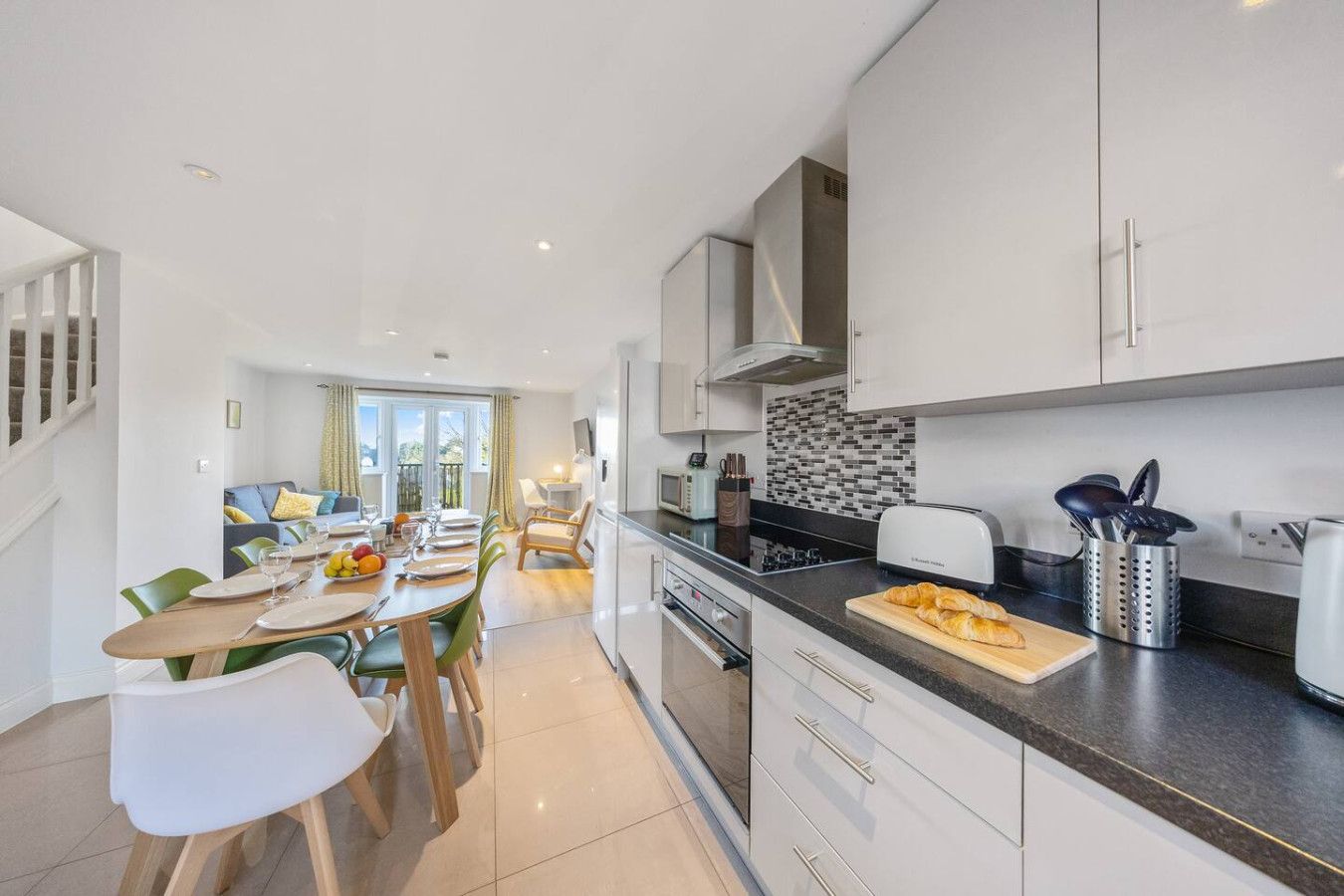 Modern kitchen with white cabinetry and dark countertops, leading into a dining area and living room with balcony doors.