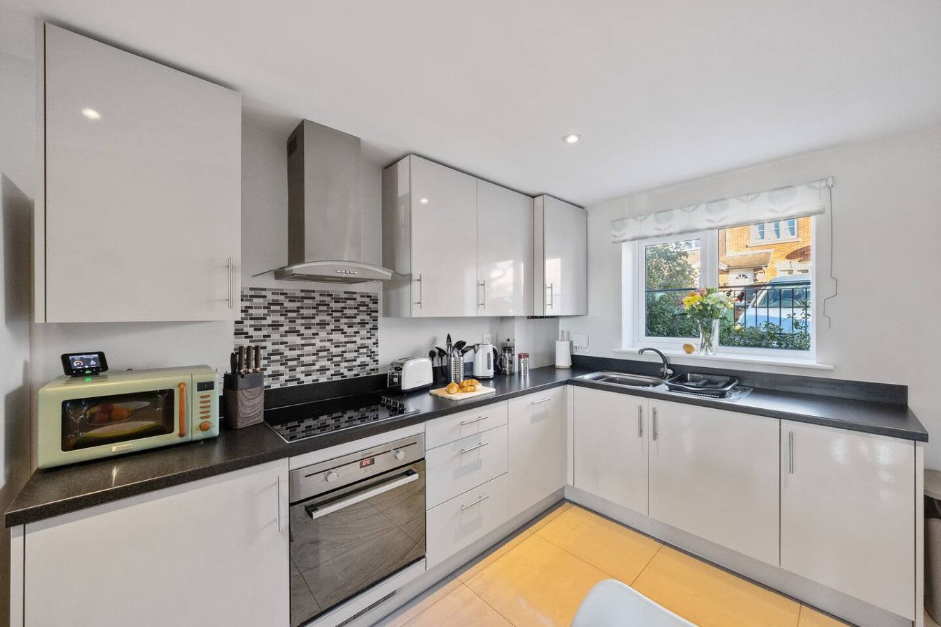 A modern kitchen with white high-gloss cabinets, stainless steel appliances, a tiled backsplash, and yellow floor tiles.