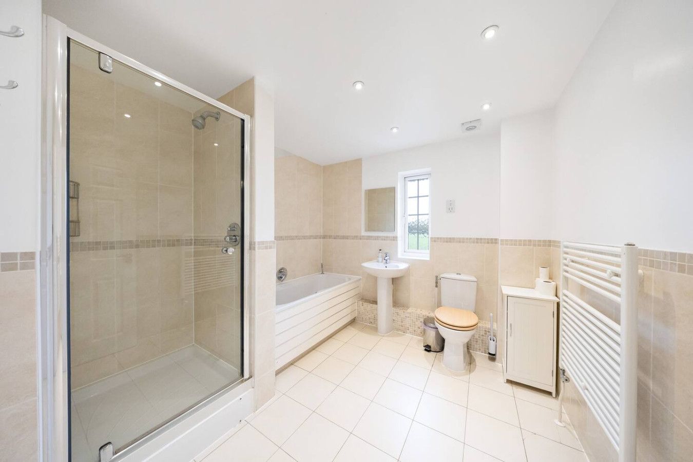 A bright, modern bathroom with a glass-enclosed shower, a bathtub, a pedestal sink, a toilet, and a white towel warmer.