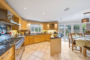 A spacious, well-lit kitchen with light wood cabinets, dark granite countertops, diagonal floor tiles, and a dining area.