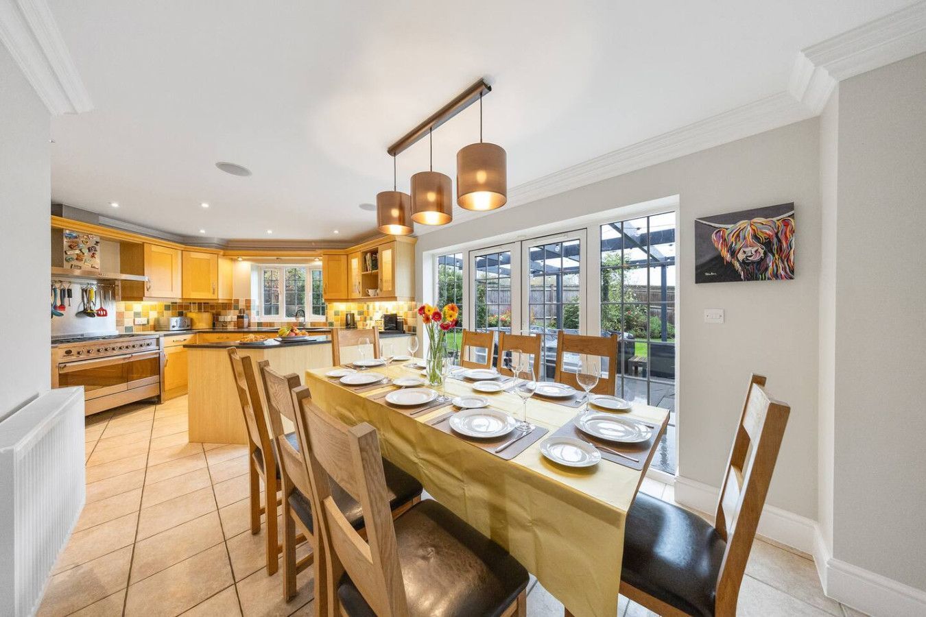 A bright, open-plan dining and kitchen area with a wooden table, chairs, and hanging pendant lights.