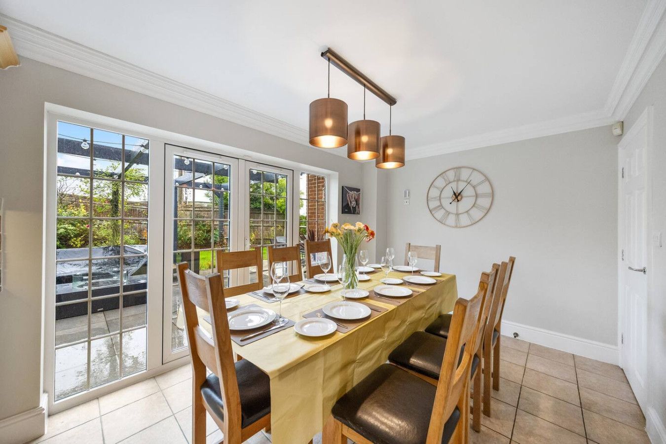 A dining room with a long table set for six, wooden chairs, a triple-pendant light, and glass doors opening to a patio.