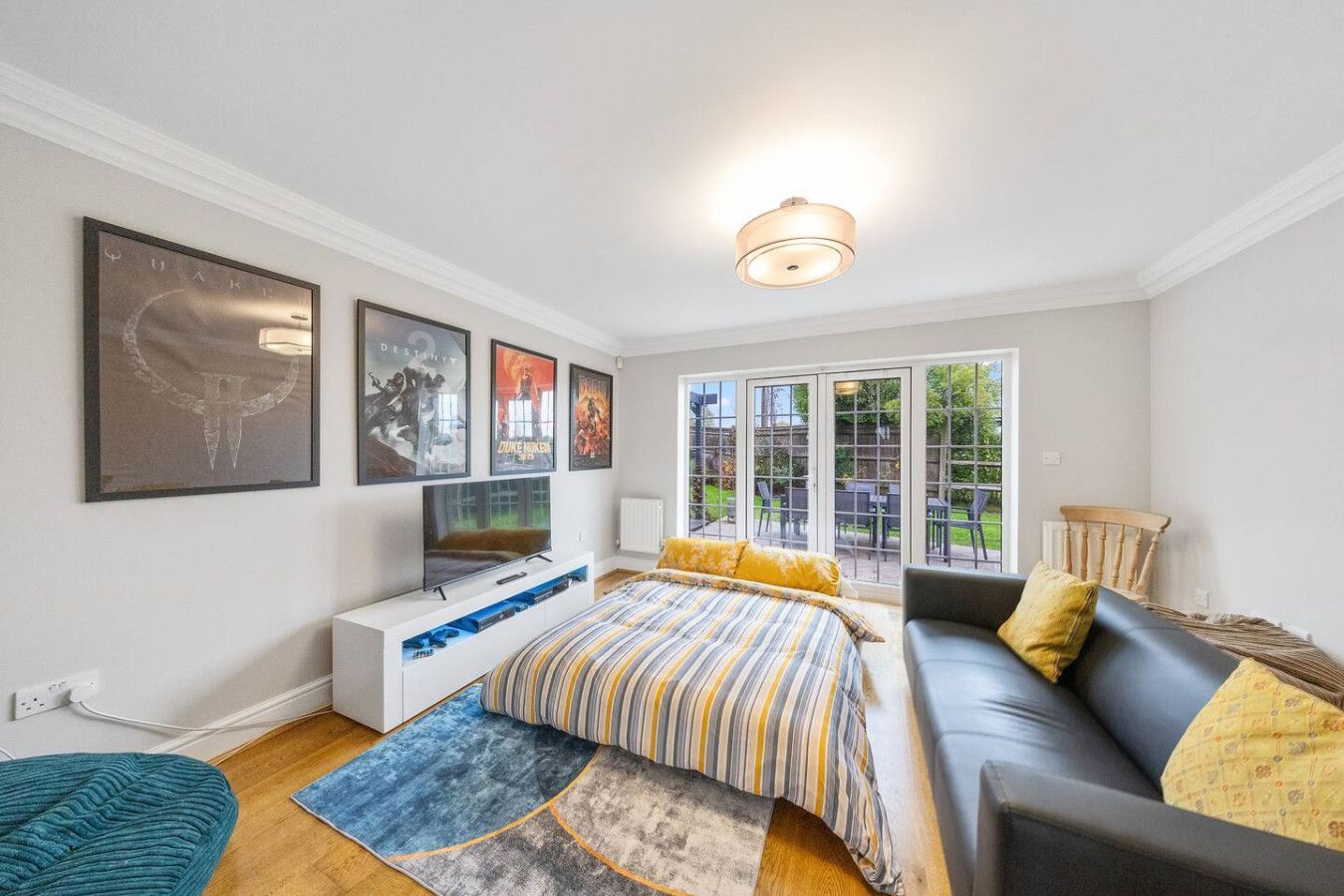 A living room with a black sofa, a striped bed, a TV on a white stand, wall art, and a glass door leading to a yard.