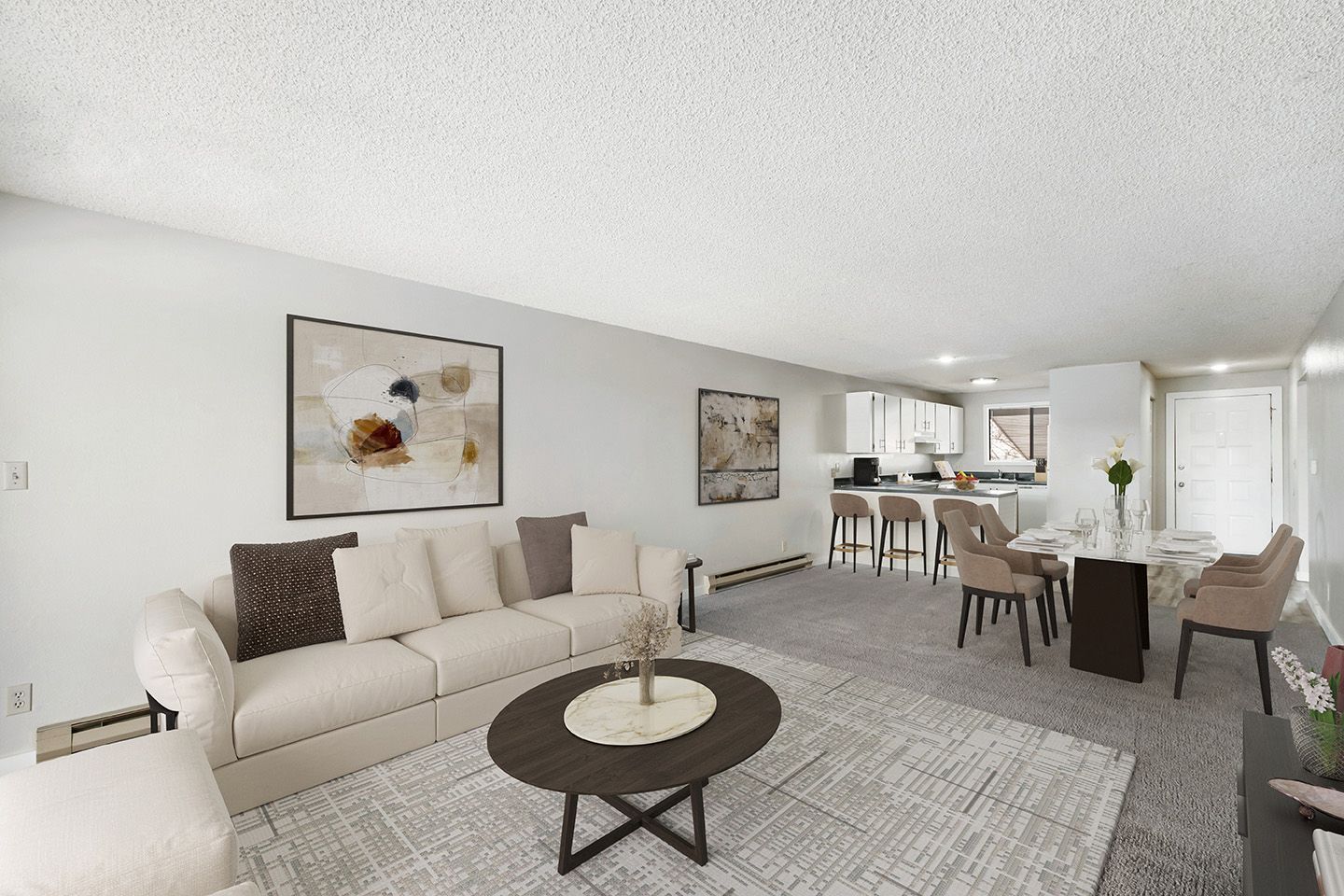 Bright open-concept living and dining room with beige sofa, round coffee table, and kitchen in background