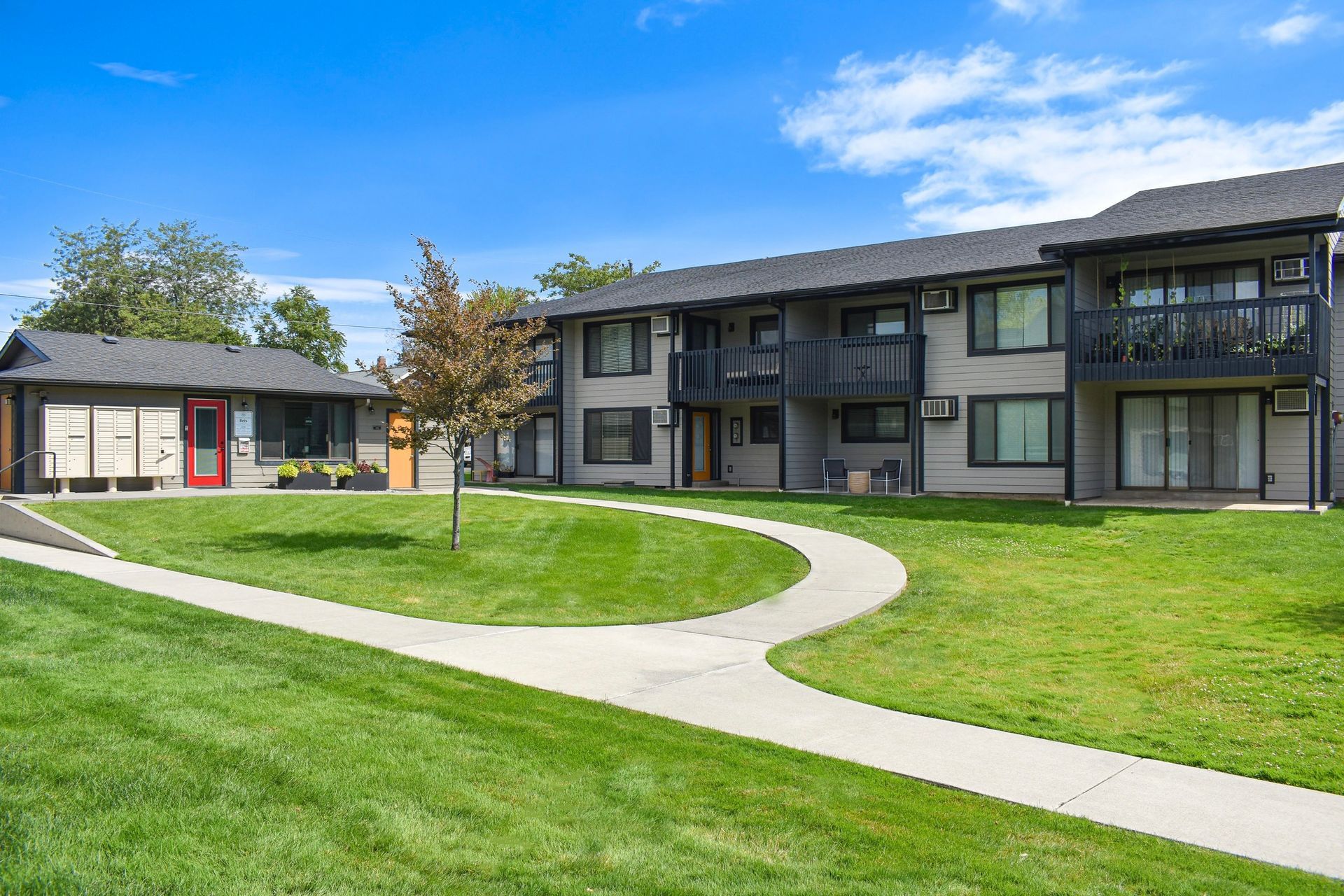 Apartment complex with curved walkway and green lawn under a clear blue sky