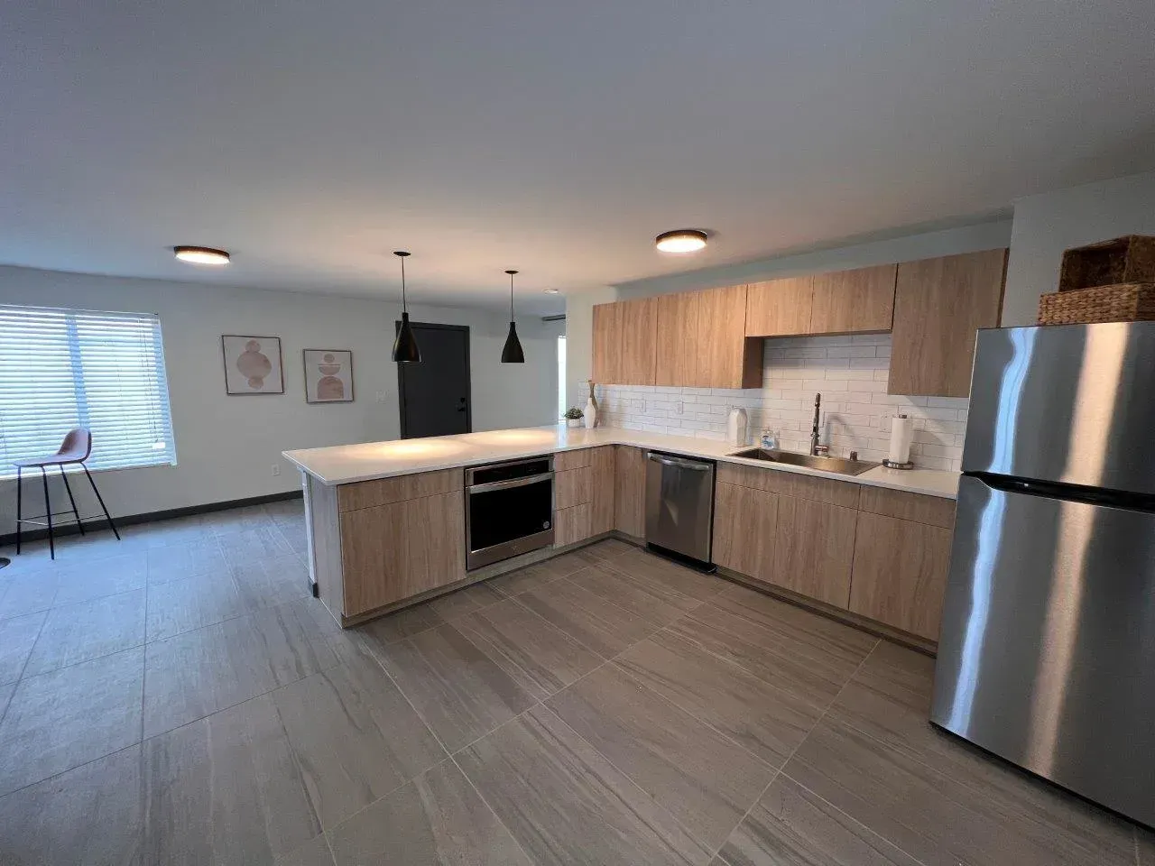 Modern open-plan kitchen with wood cabinets, stainless steel fridge, island, and adjacent dining area