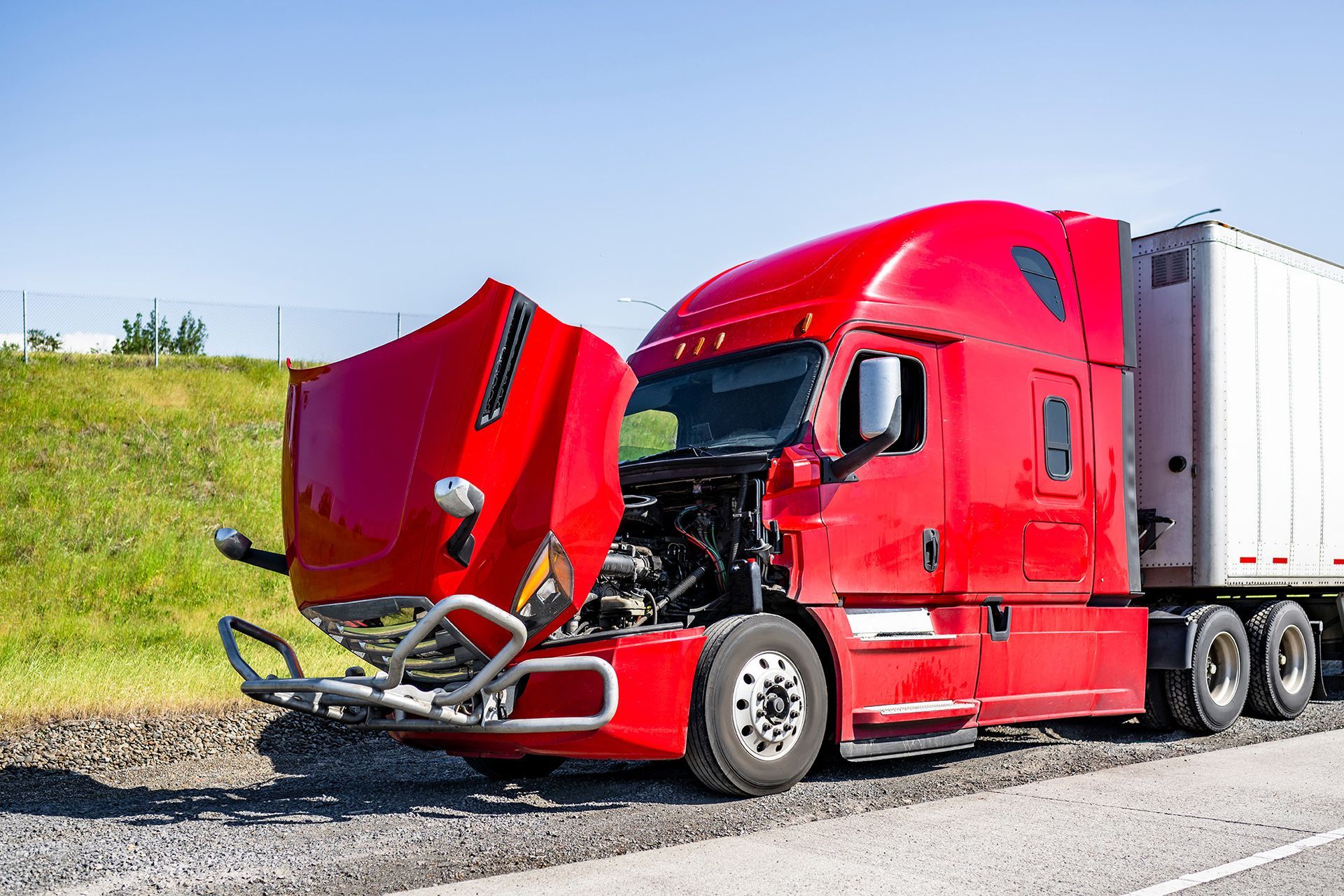 Red semi-truck with open hood on the side of a road, appearing broken down, with a white trailer.