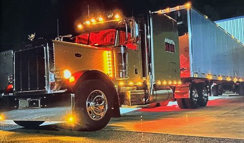 Semi-truck with illuminated lights at night. Trailer attached, red and amber lights visible.