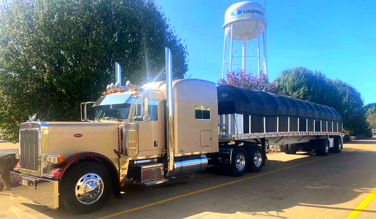 Gray semi-truck with a white trailer parked on the side of a road, with a blue sky in the background.