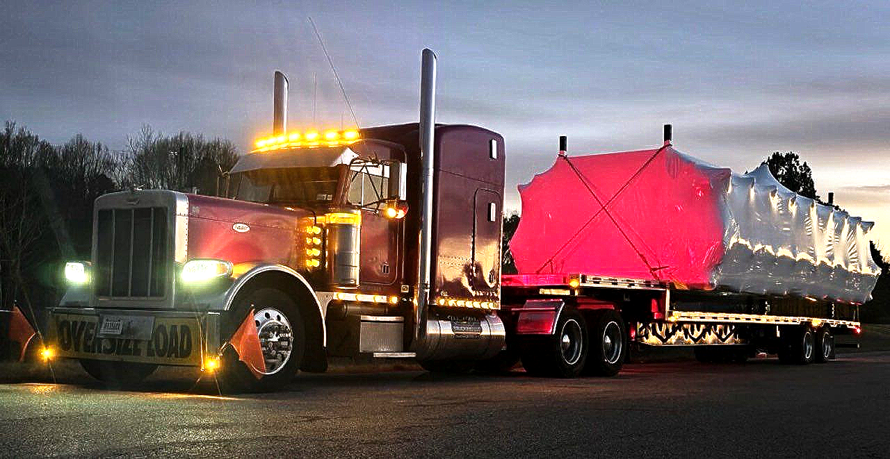 Two men shaking hands in front of a tanker truck, both smiling. One in a safety vest holds a clipboard.