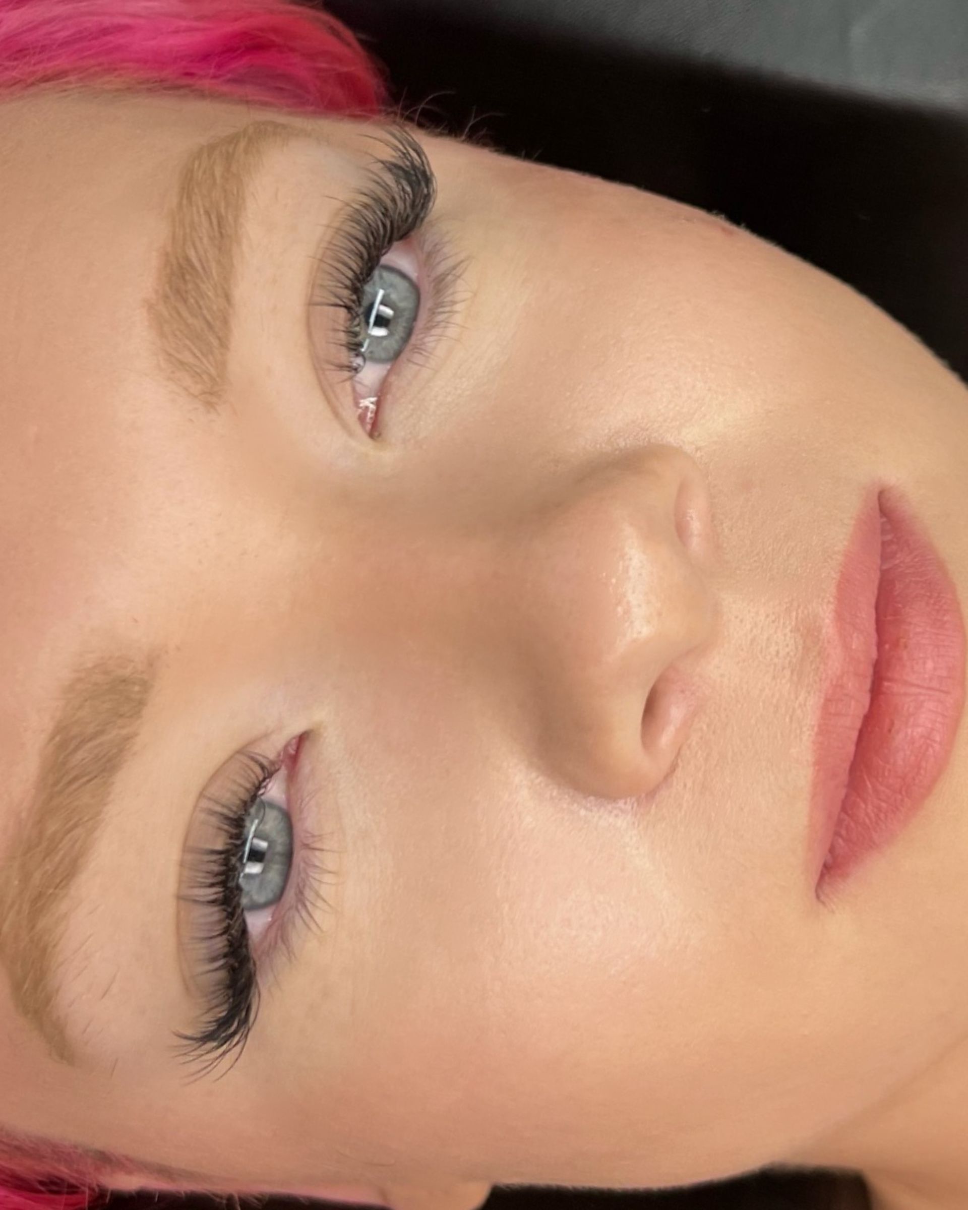 A close up of a woman 's face with pink hair and blue eyes.