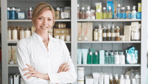 A female pharmacist is standing in front of a shelf full of cosmetics.