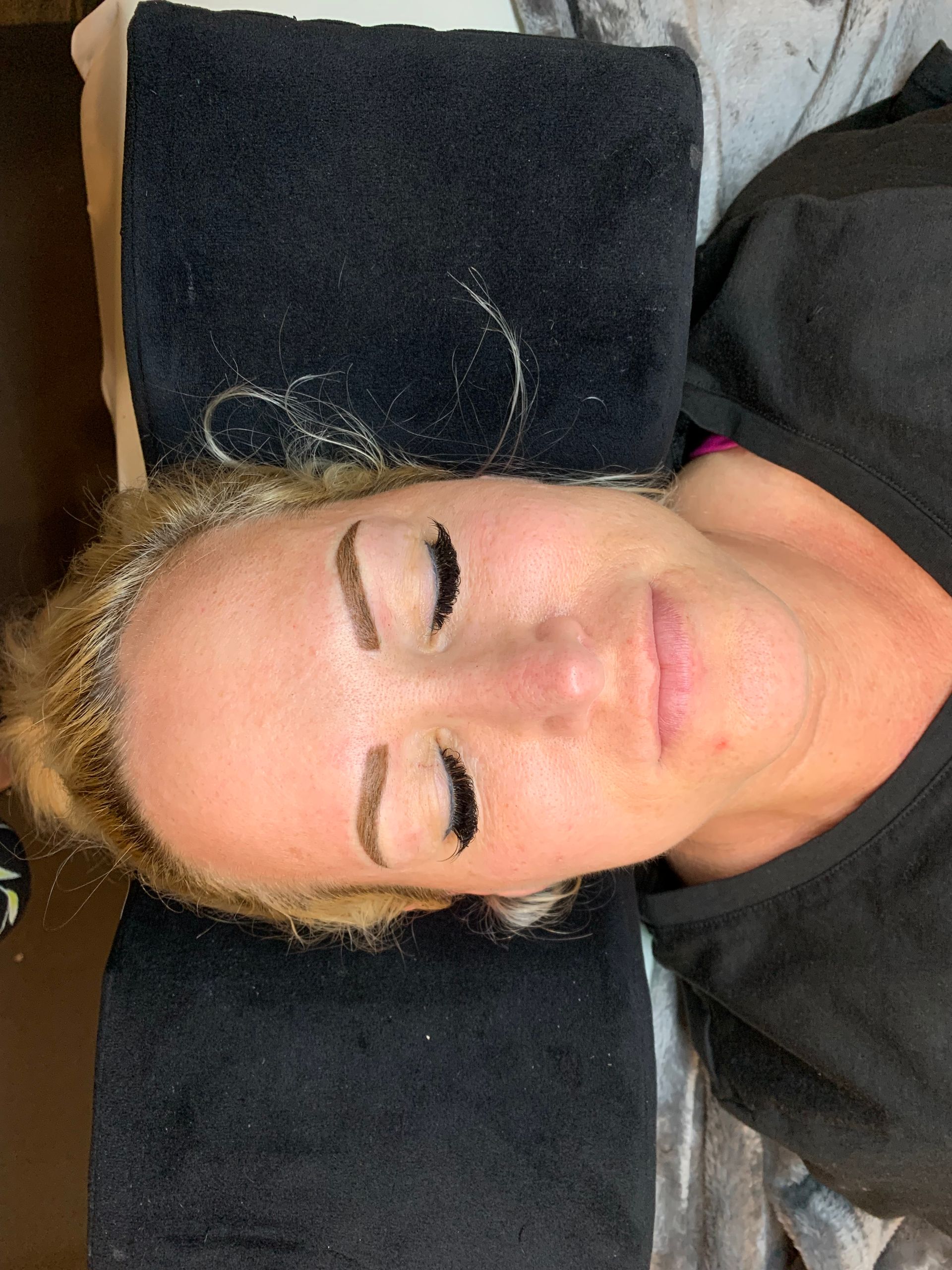 A woman is laying on a bed with her eyes closed and a towel on her head.