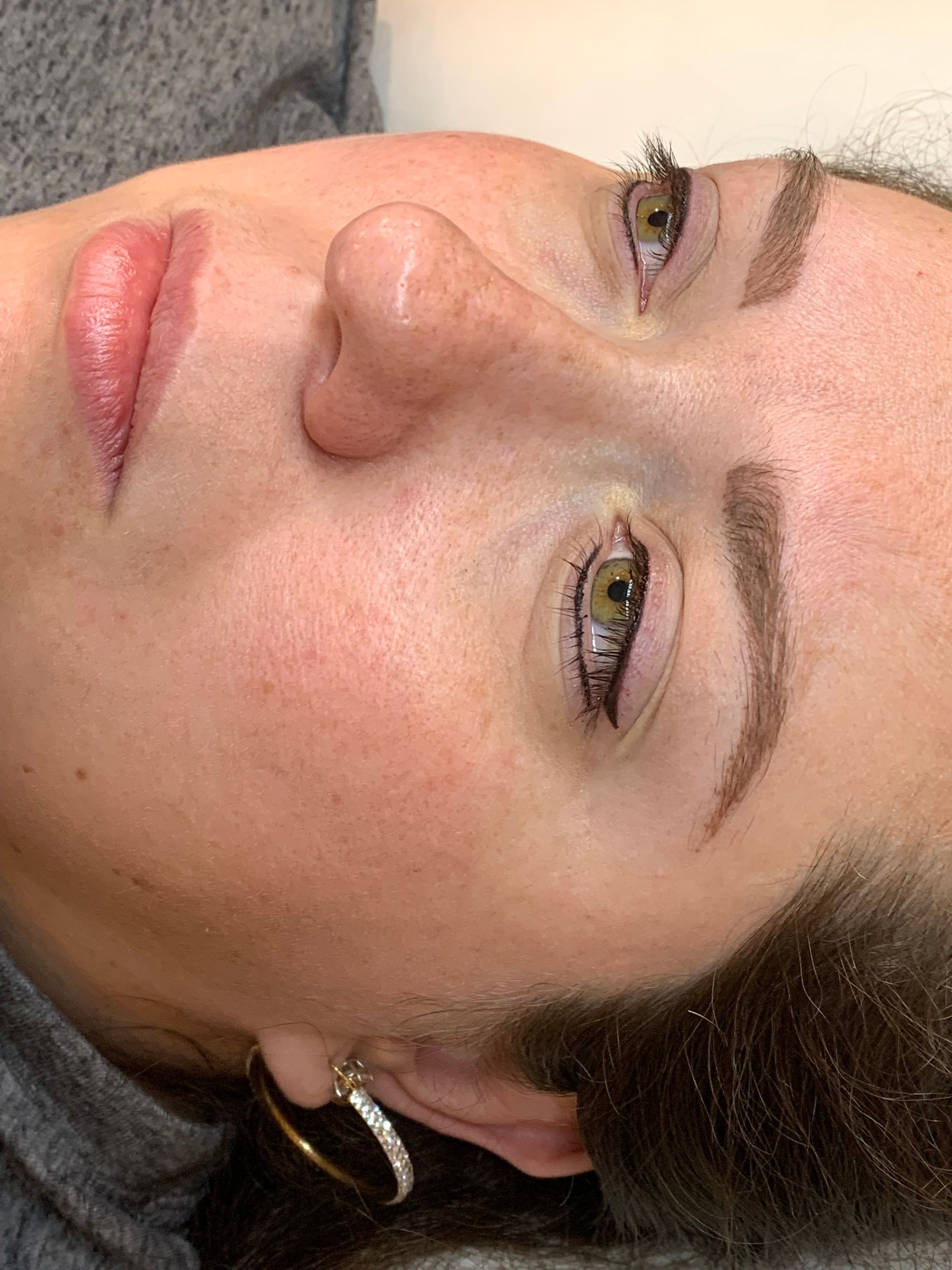 A close up of a woman 's face with a gray sweater and earrings.