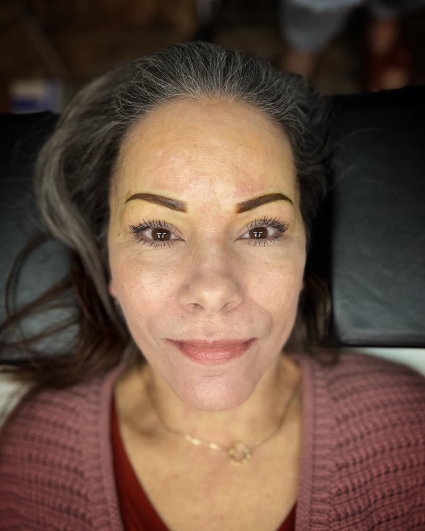 A close up of a woman 's face with gray hair and a pink sweater.