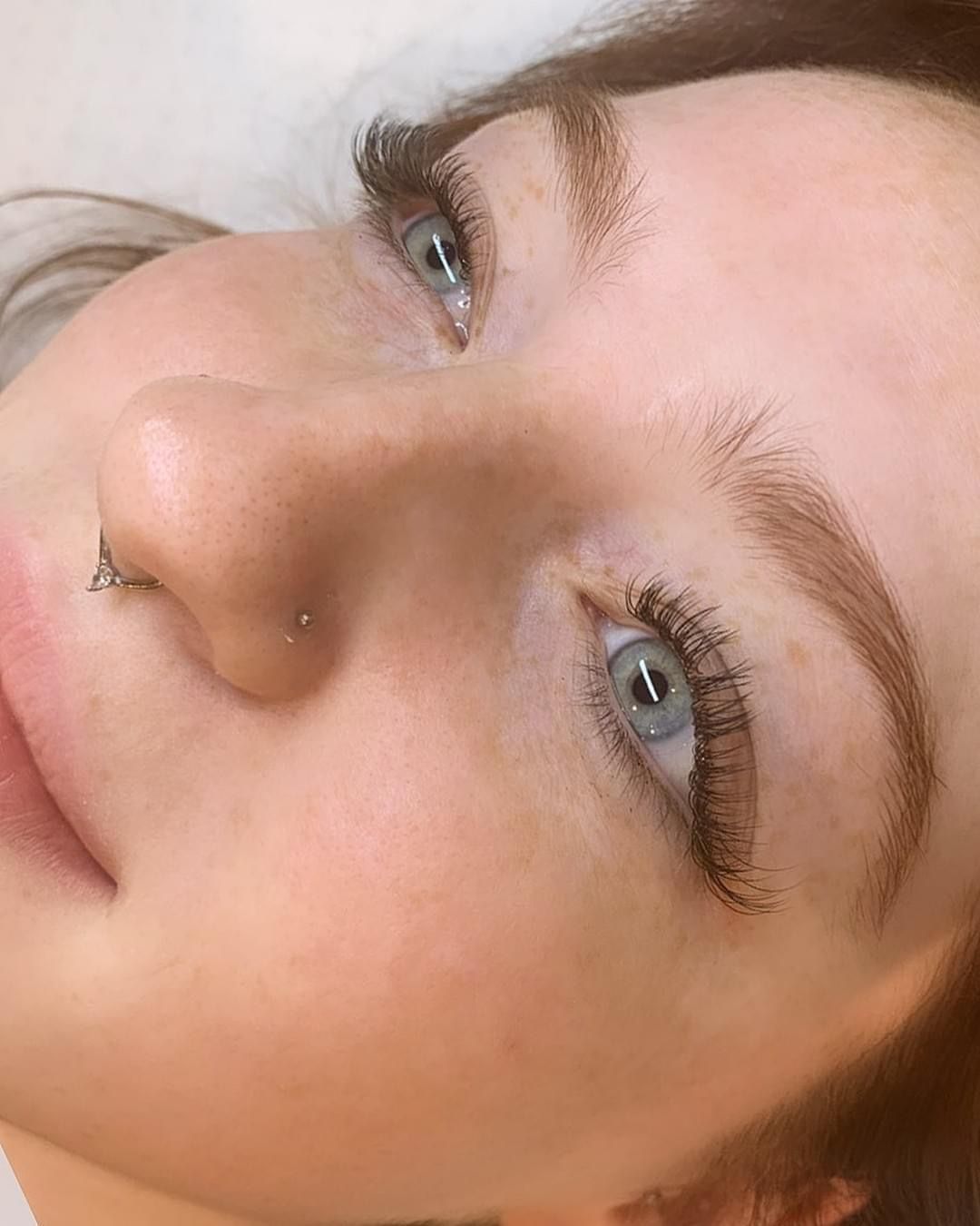 A close up of a woman 's face with long eyelashes and a nose ring.