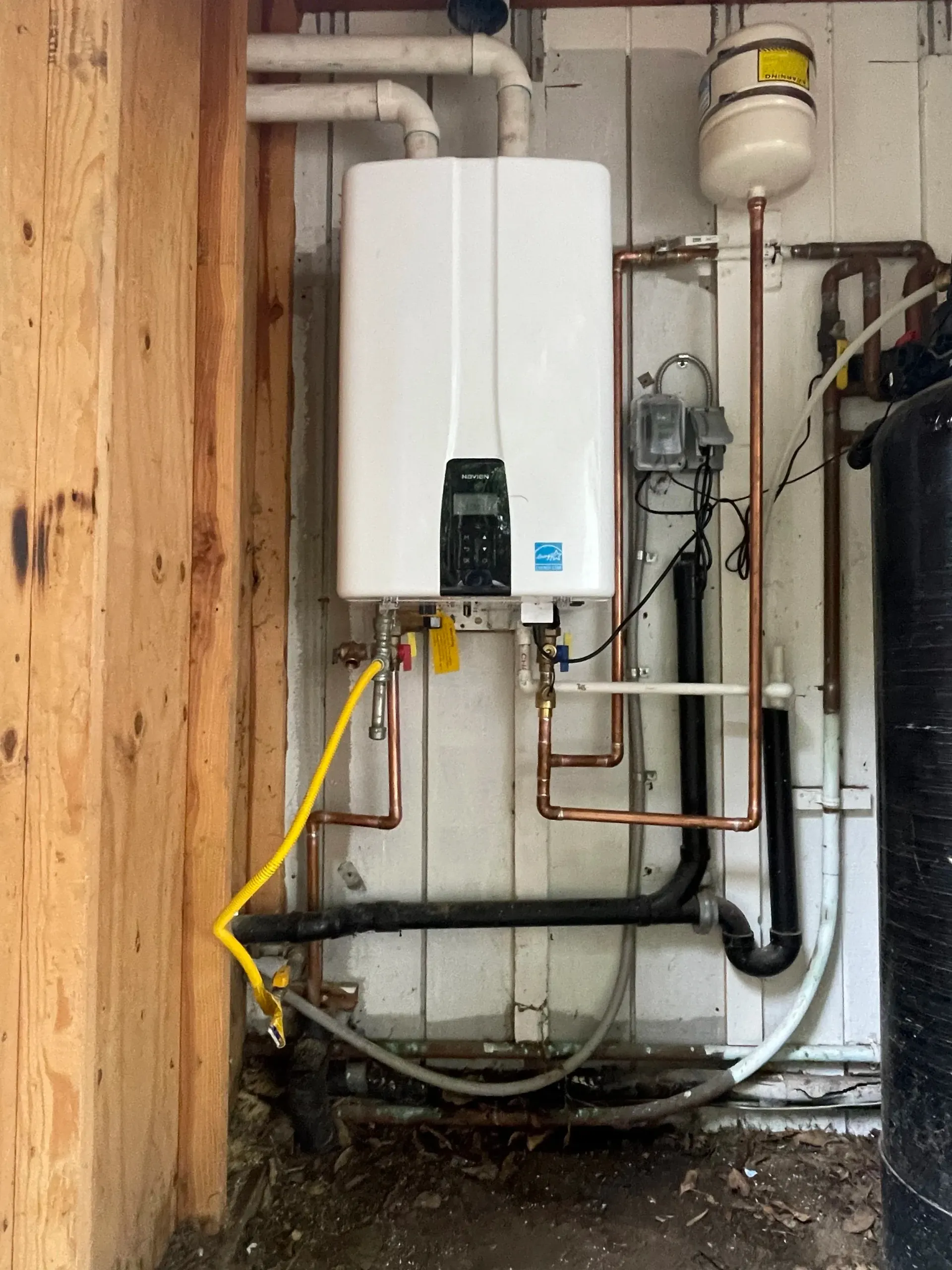 A Rheem furnace in a basement, with white pipes, grey metal, and a treadmill.
