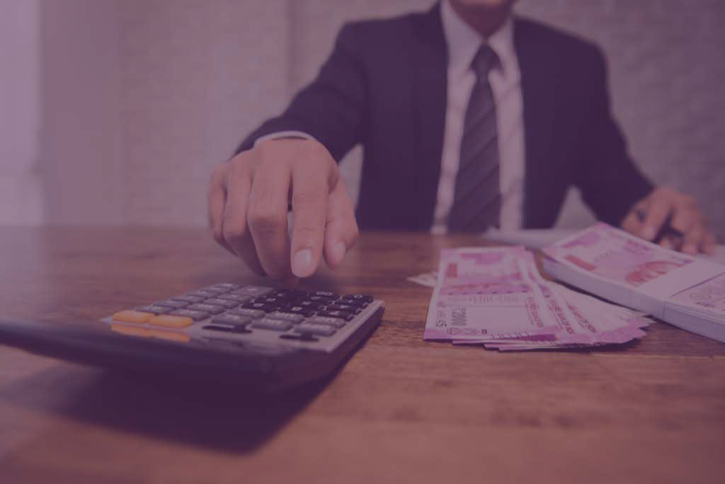 A man in a suit and tie is sitting at a table using a calculator.